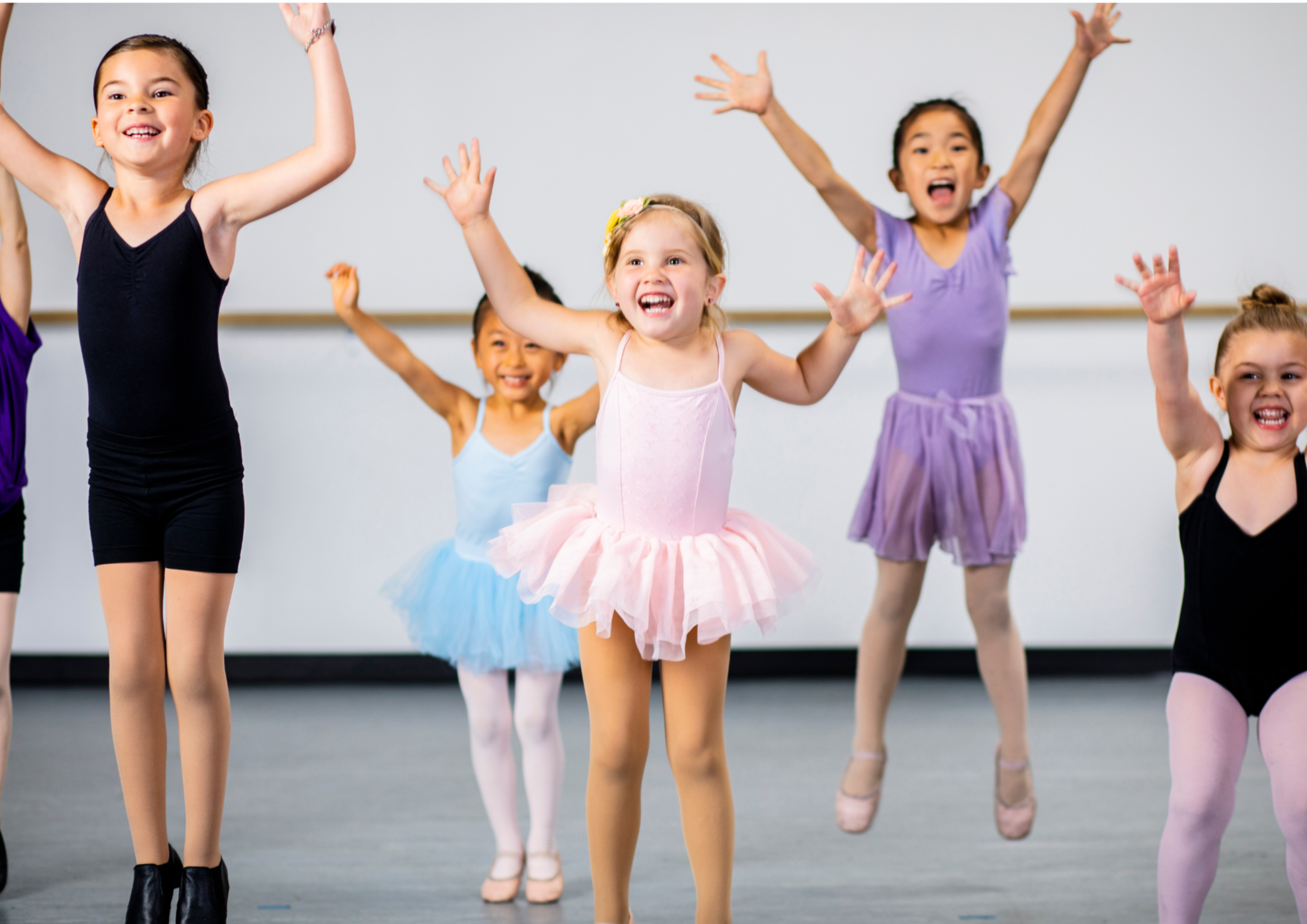Group of young girls in ballet tutus and leotards jumping with arms raised in a dance studio in Grey Lynn, Auckland.
