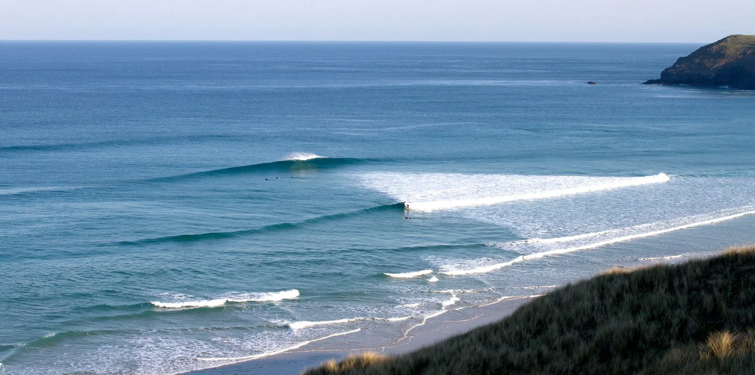 Ocean waves with surfers and a hillside in the background.