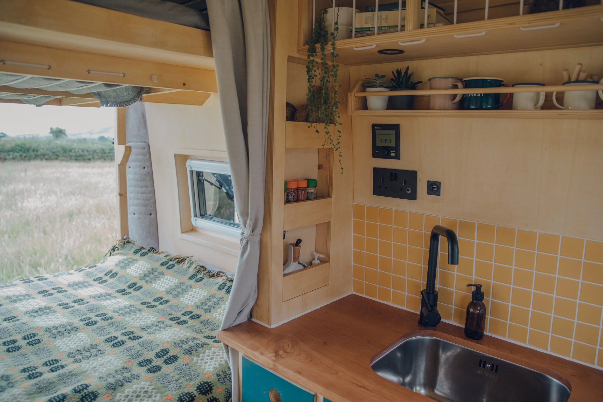 Campervan conversion based in devon with yellow kitchen tiles, fixed bed with clever storage. Bunk bed for children, hot water and heating system controls