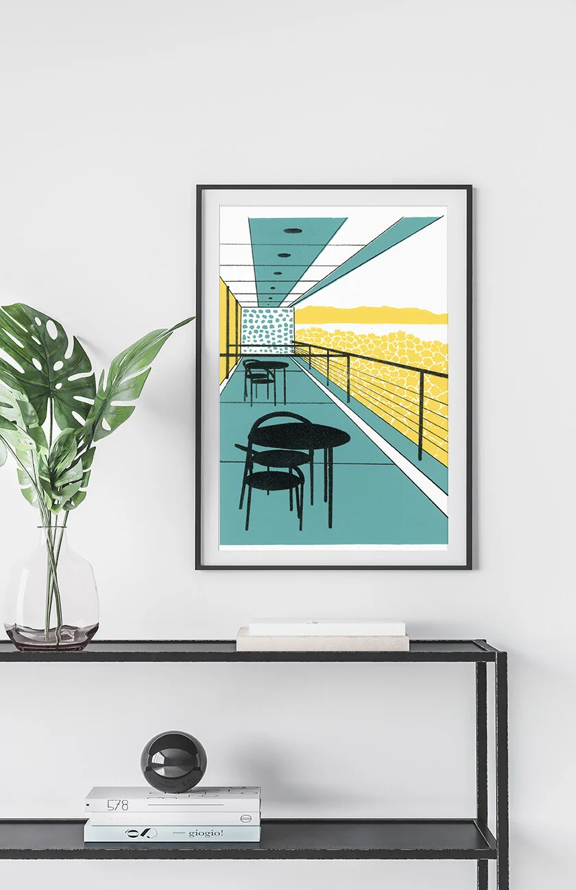 Framed print of a modern balcony scene displayed in a minimalist interior above a console table with books and a vase.