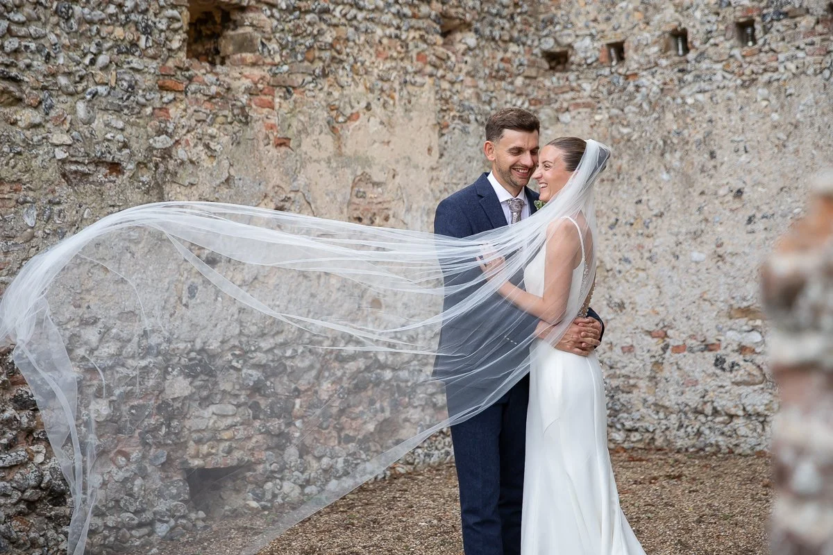 Bride and Groom in ruins with a veil blowing in the wind at a Norfolk Wedding Venue