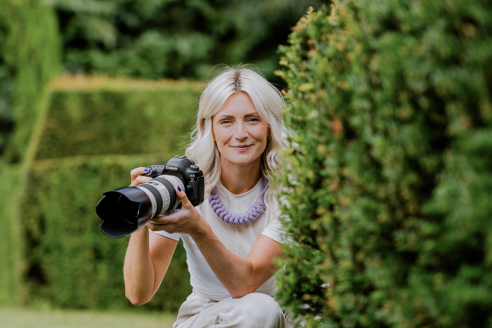 Photo of Emma Cullen holding a 70-200mm lens in the grounds of a Wedding Venue in Norfolk, she's smiling at the camera and it's summertime