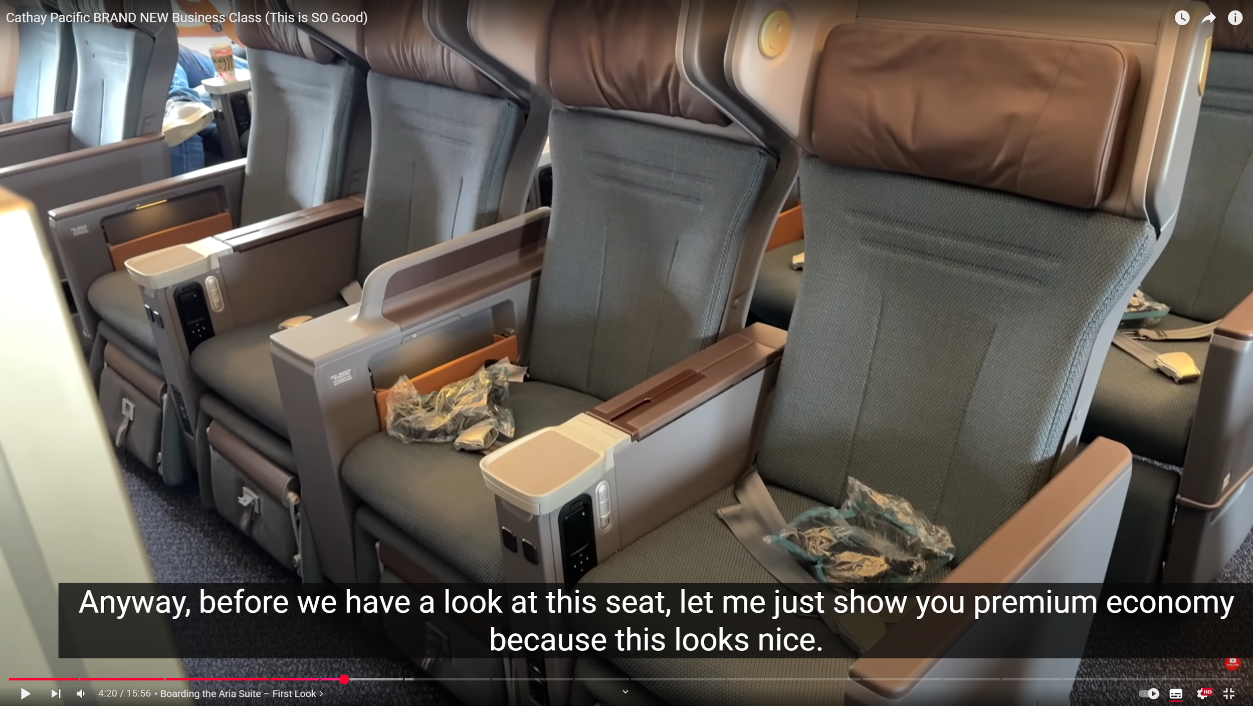 Photo of three economy class airplane seats with gray upholstery, adjustable headrests, and built-in entertainment screens. Plastic packaging and personal items are on some seats.