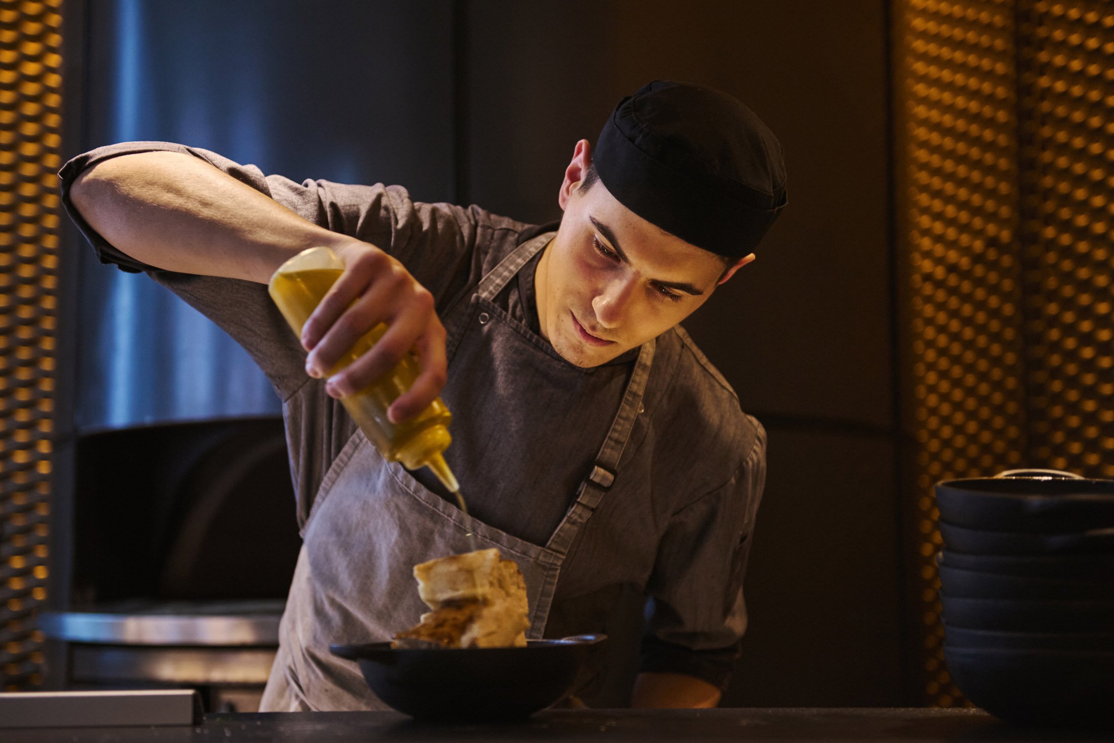 Chef pouring oil on food on a plate. Lifestyle photographer London.