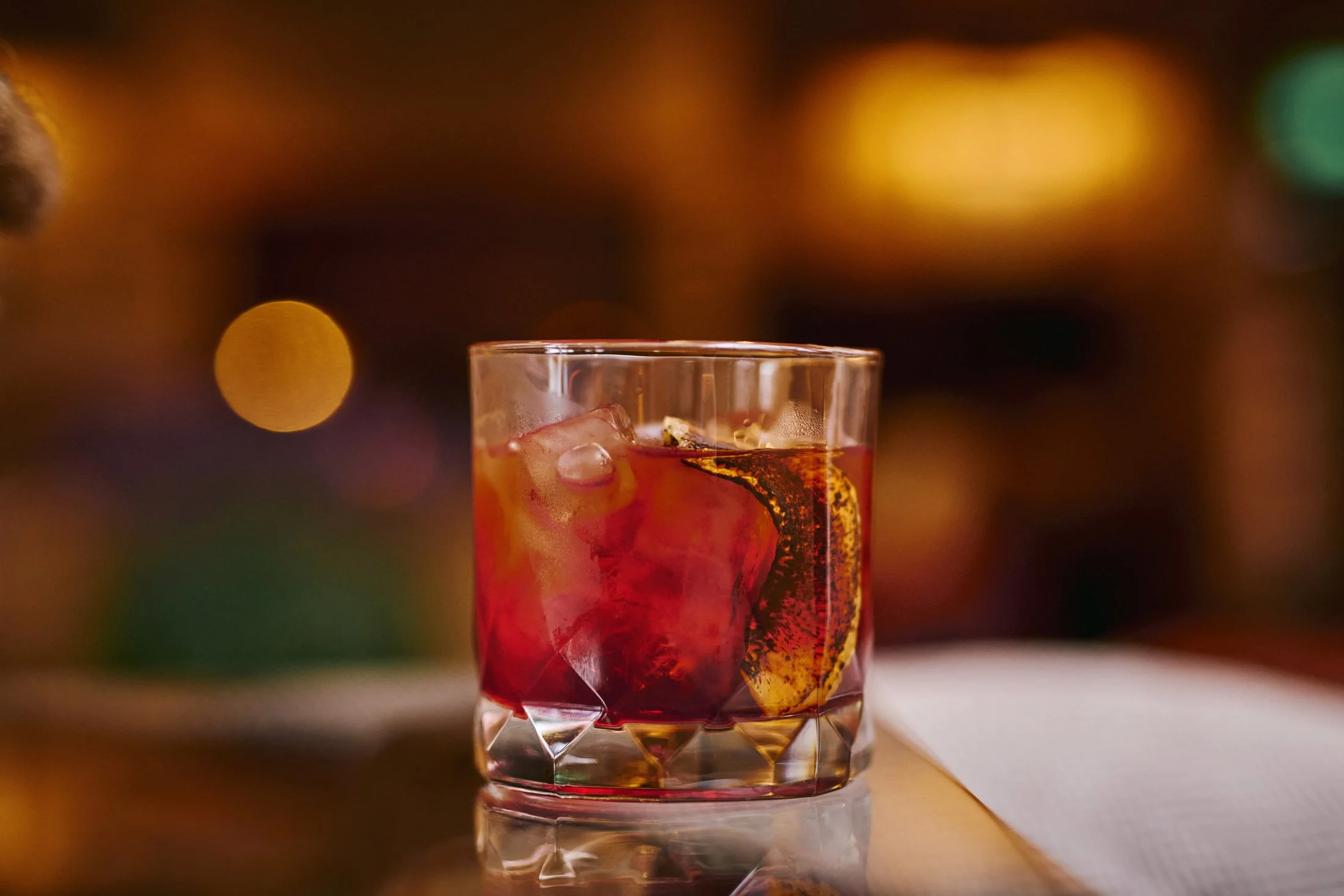 Glass of cocktail with ice and orange twist on table. Lifestyle photographer London.