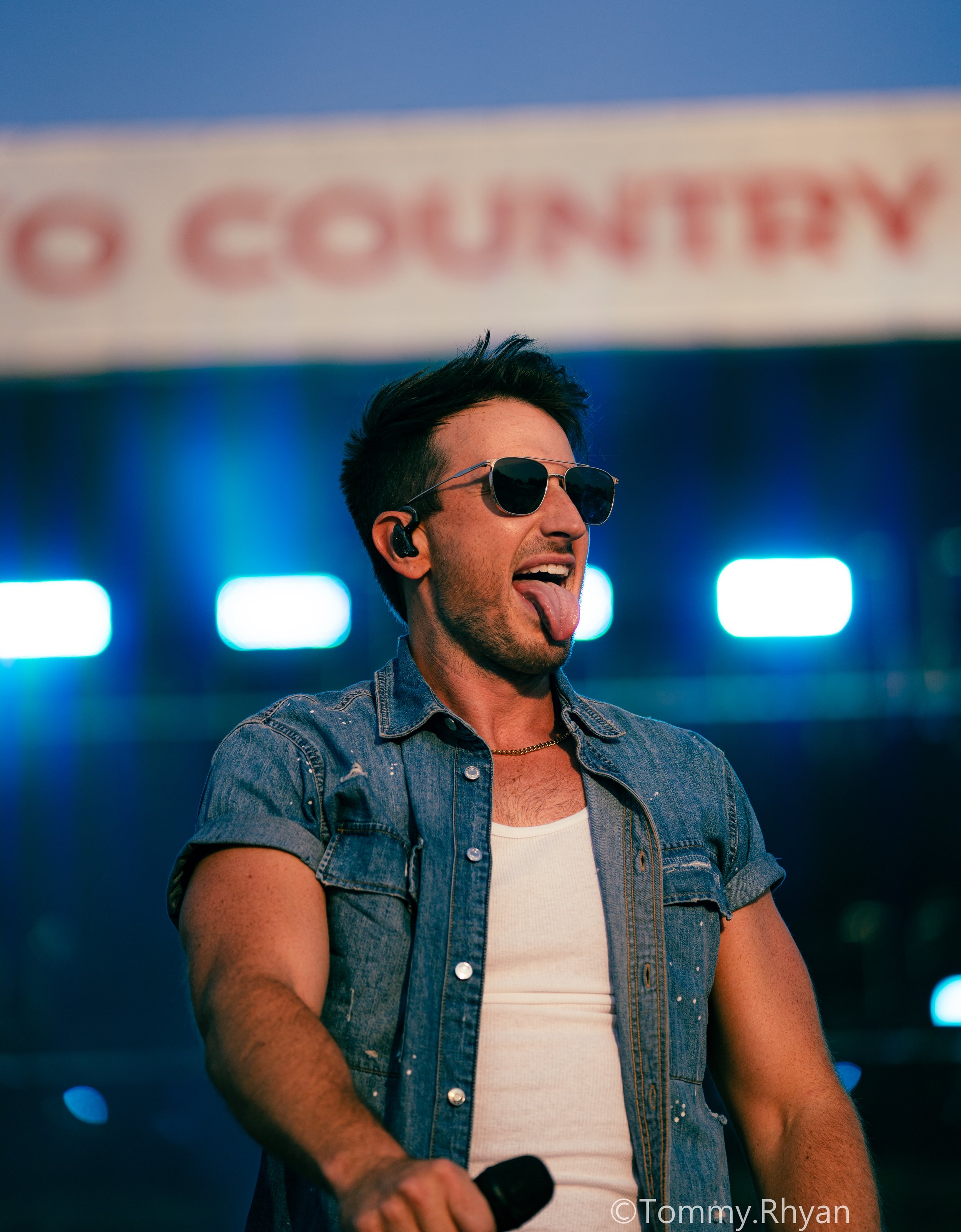 Man in denim shirt performing on stage with microphone
