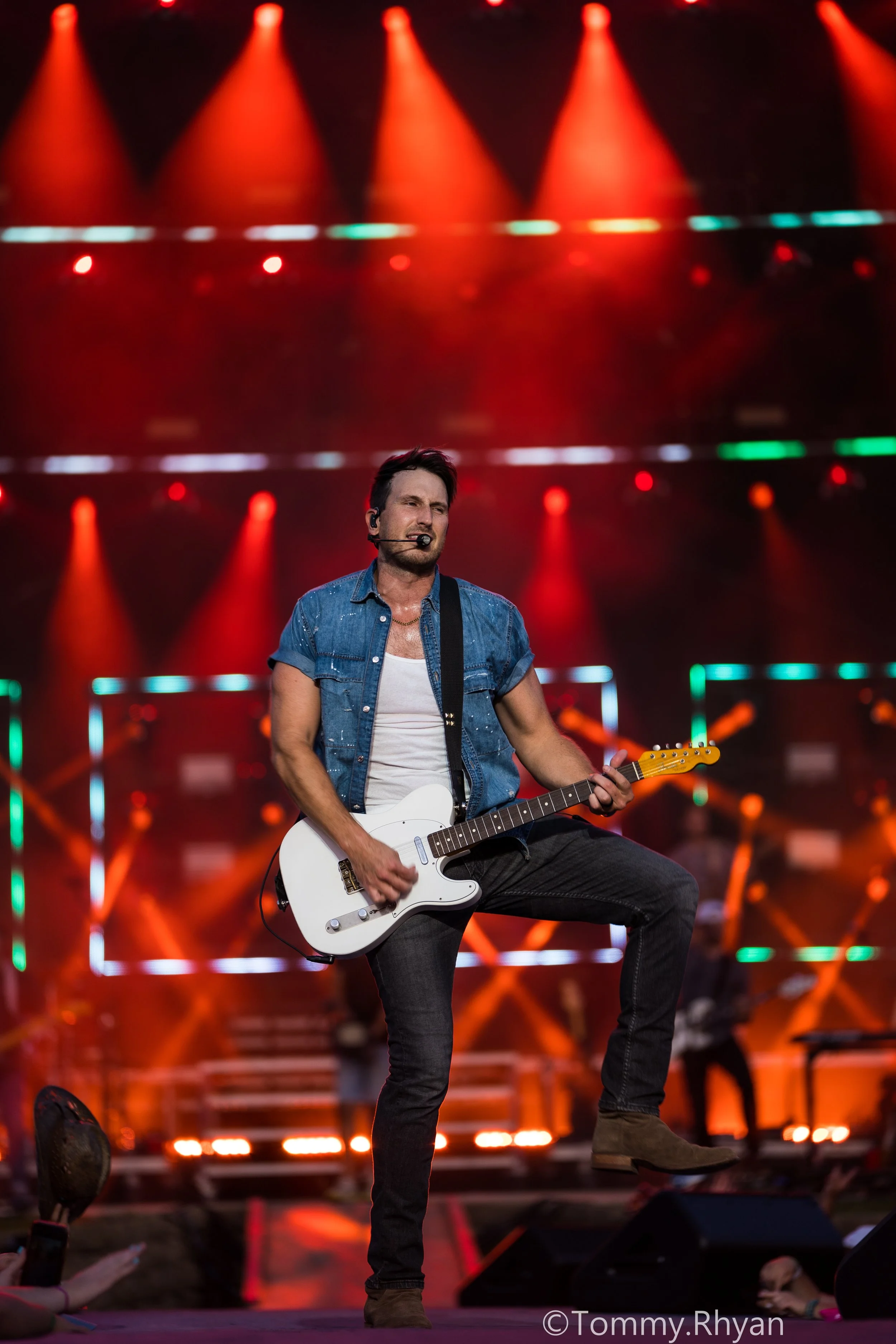 Musician playing guitar on stage under orange lights.