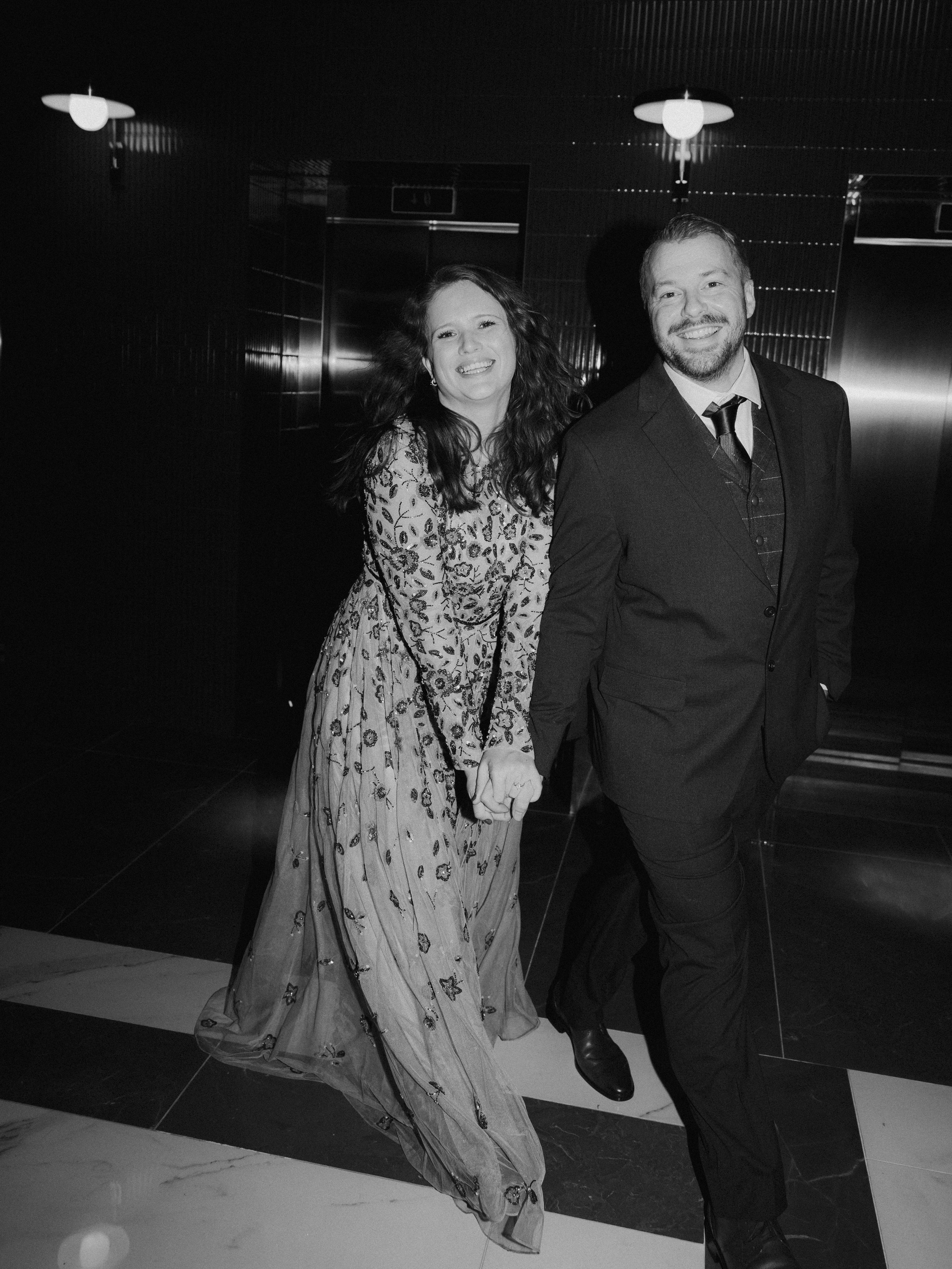 Bride and groom holding hands and smiling in a hotel hallway after their Natural History Museum elopement in London.