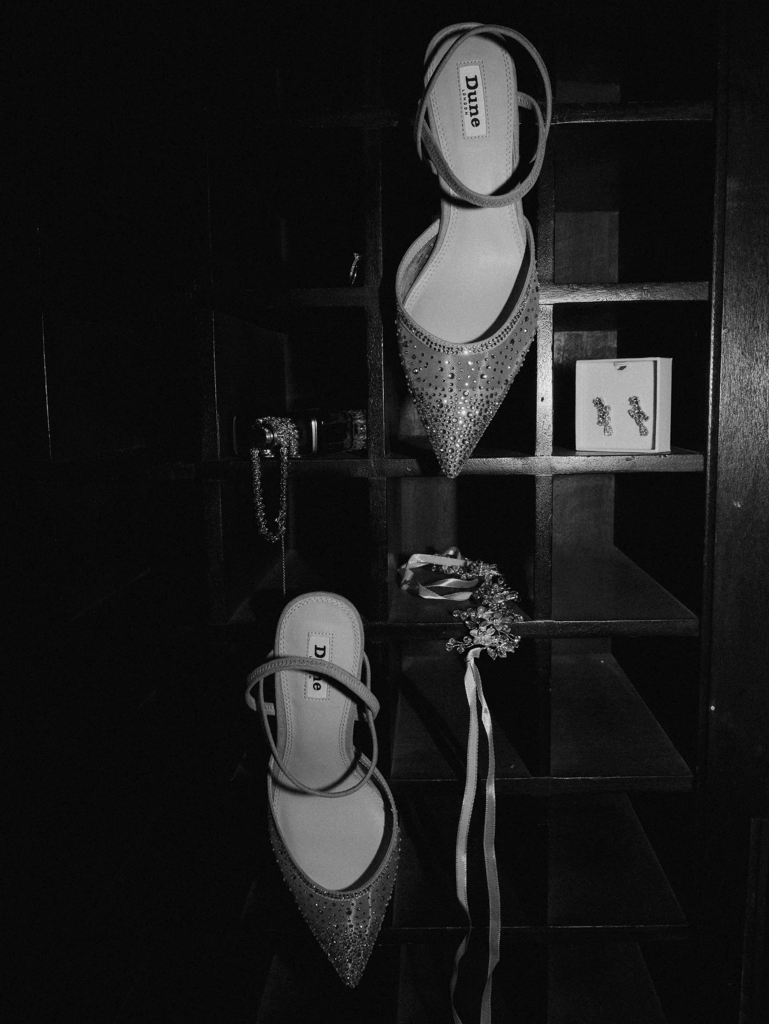 A black and white image of a bride's shoes and jewellery ahead of her wedding day.