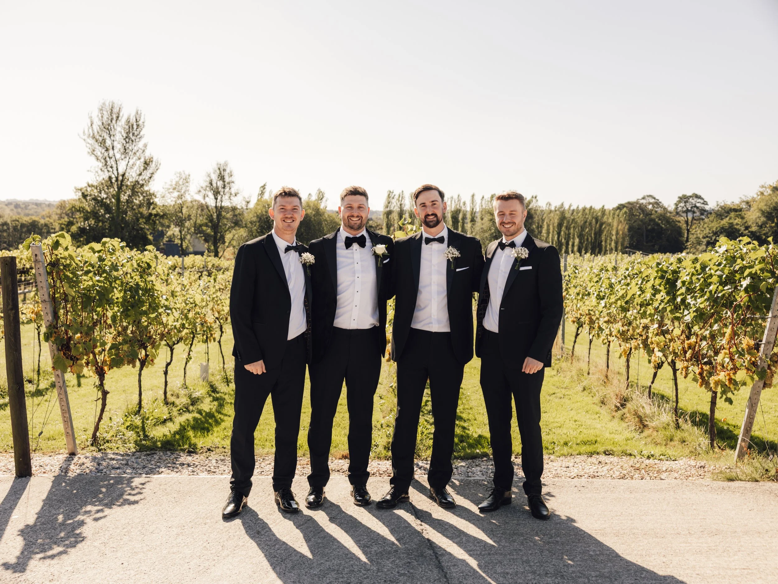 Groom and groomsmen in black tuxedos at a relaxed summer wedding at Llanerch Vineyard in South Wales