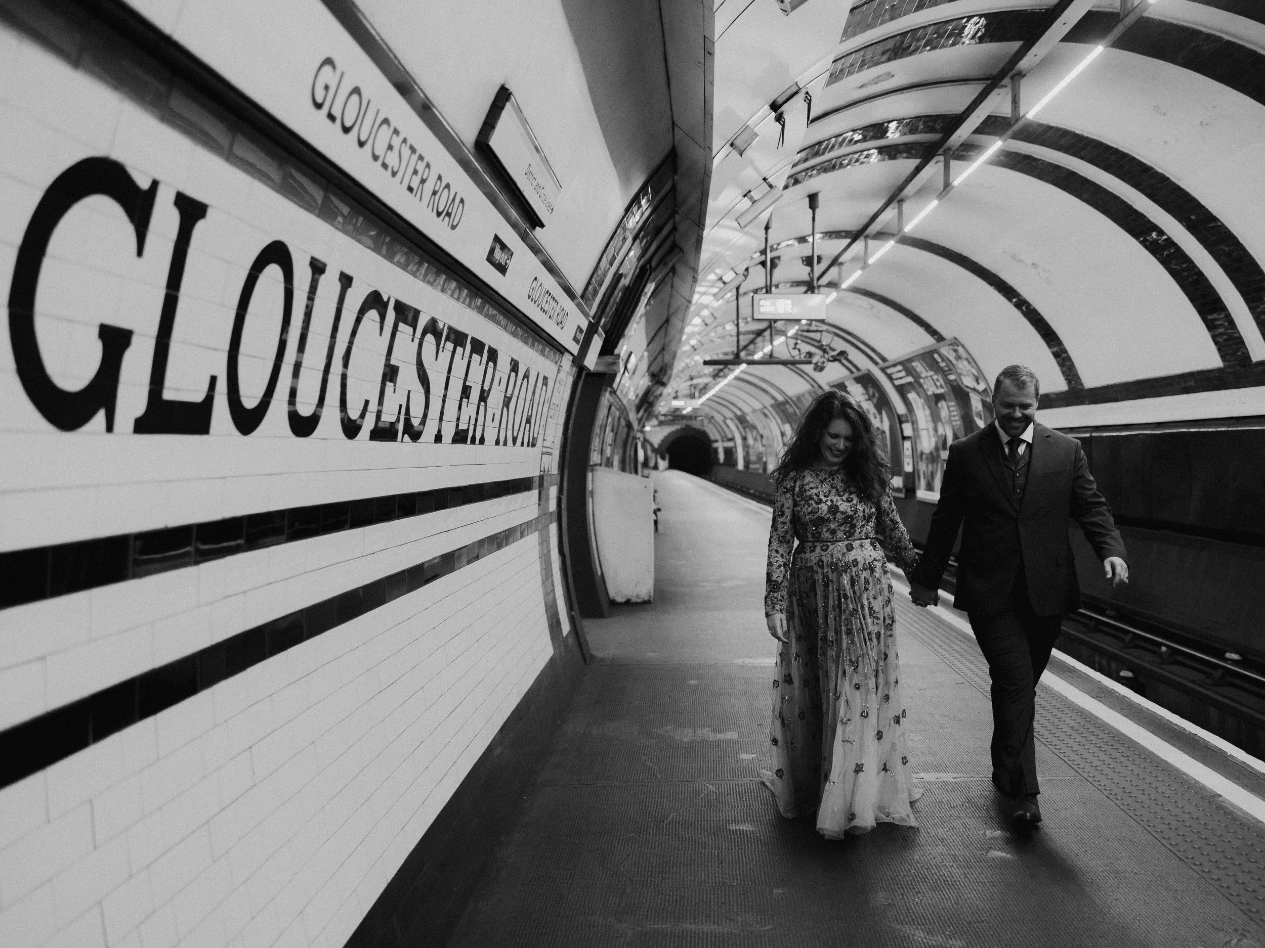 Bride and groom walking hand in hand through Gloucester Road Underground station in London on their elopement day.