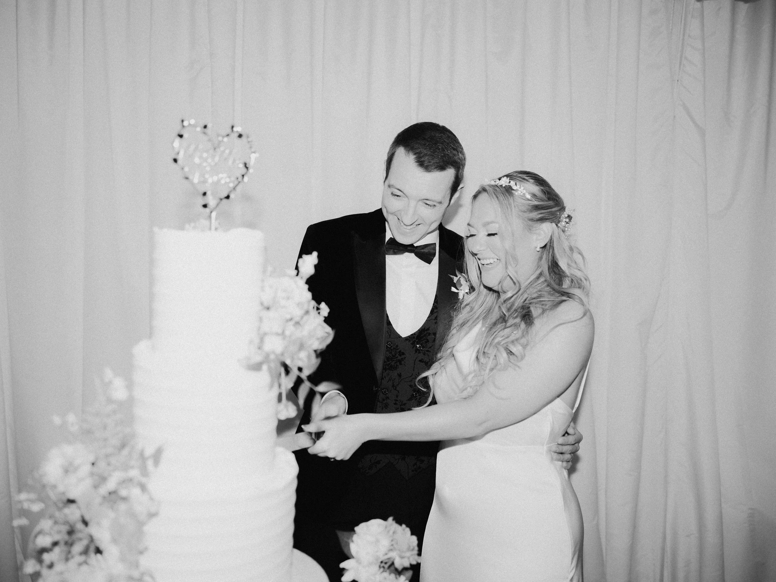 A black and white image of a bride and groom cutting their wedding cake.