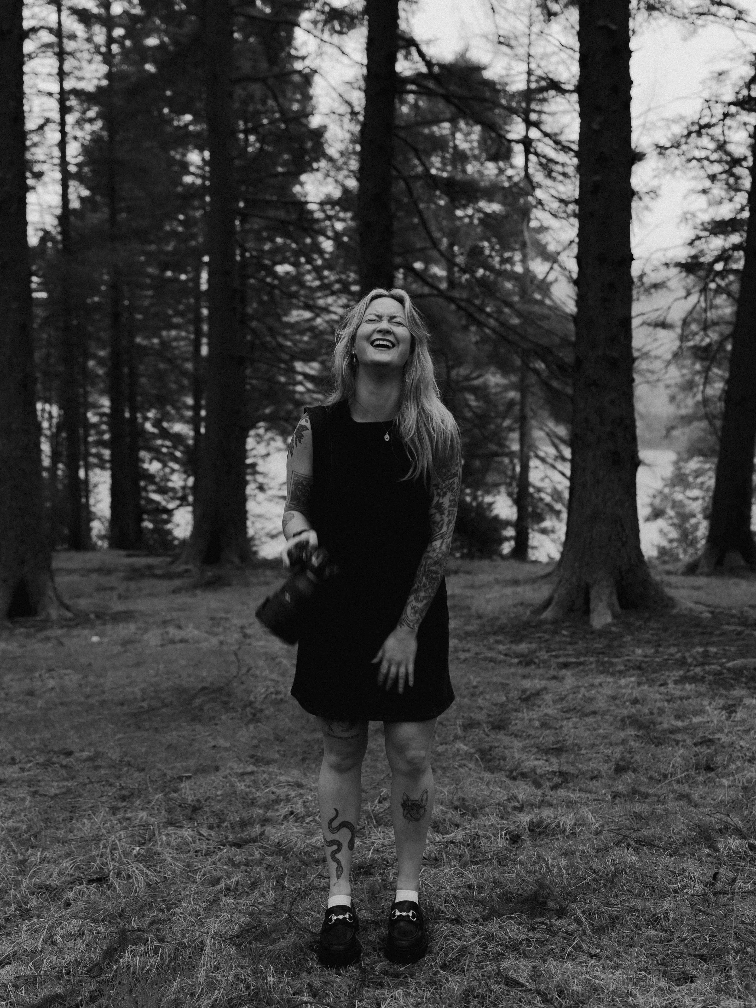 Relaxed outdoor headshot of a South Wales wedding photographer laughing in a wooded setting, holding a camera.