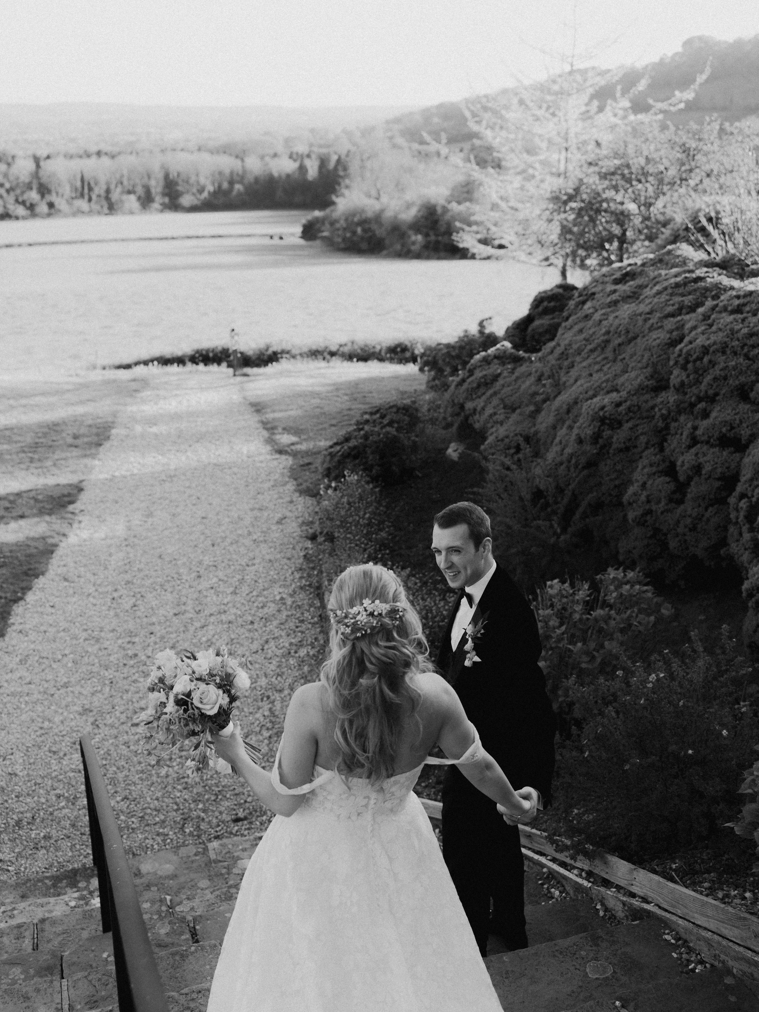 A candid image in black and white of a bride and groom descending the staircase at their venue.
