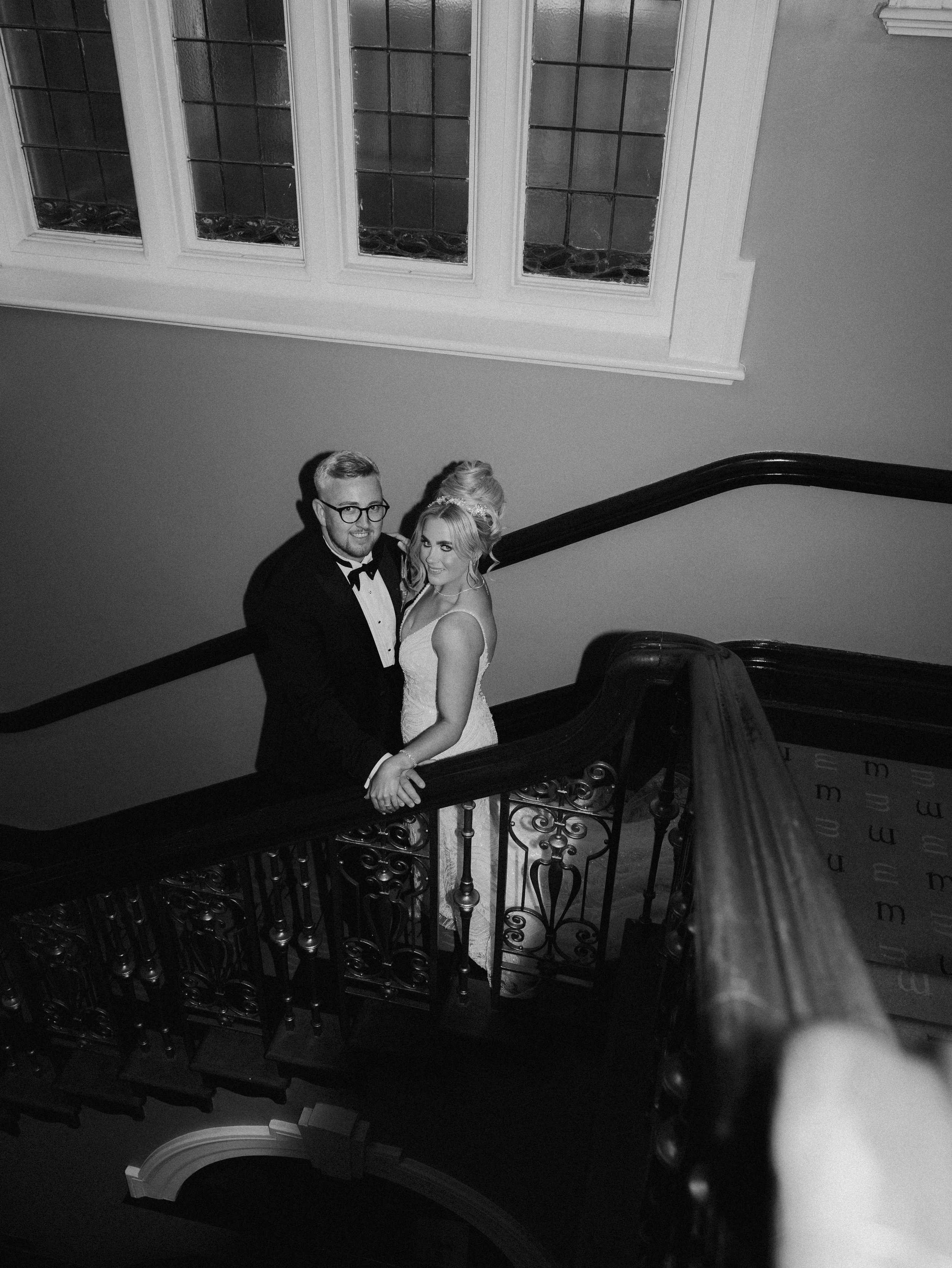 A black and white portrait image of a bride and groom embracing on the stairs at their wedding venue Morgans Hotel in Swansea.