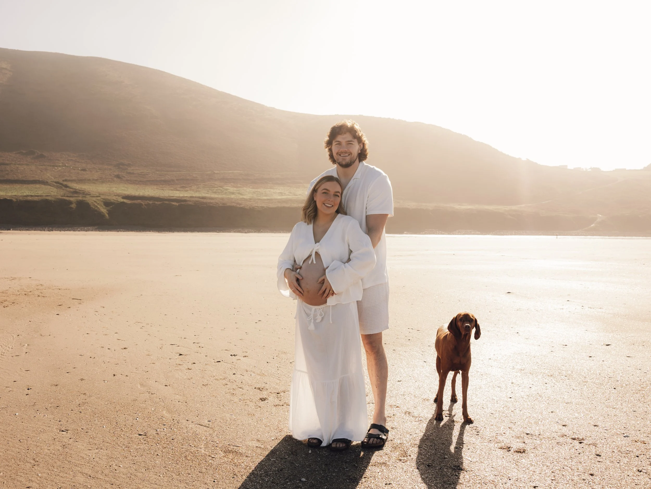 Pregnant woman and her partner with their dog on the beach in South Wales
