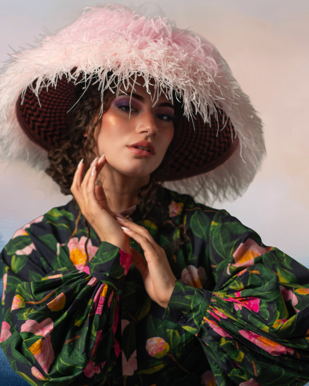 A woman with curly hair wearing a large pink and white fluffy hat and a floral-patterned blouse.