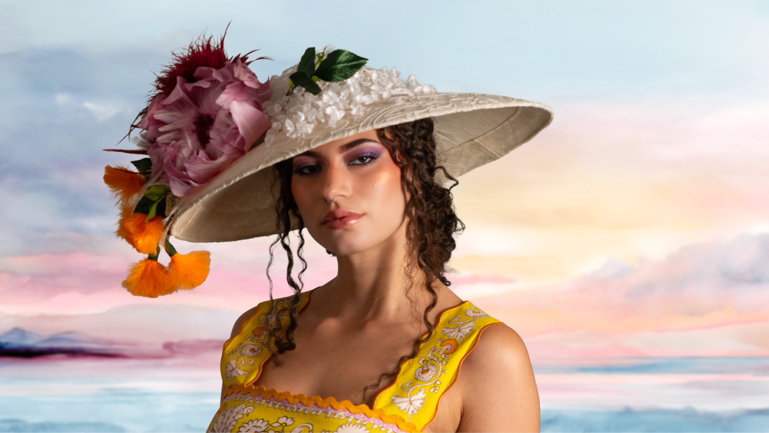 A woman wearing a large, decorated sun hat with pink flowers, orange feathers, and green leaves, standing against a colorful sky with pink and blue clouds, dressed in a yellow embroidered dress.