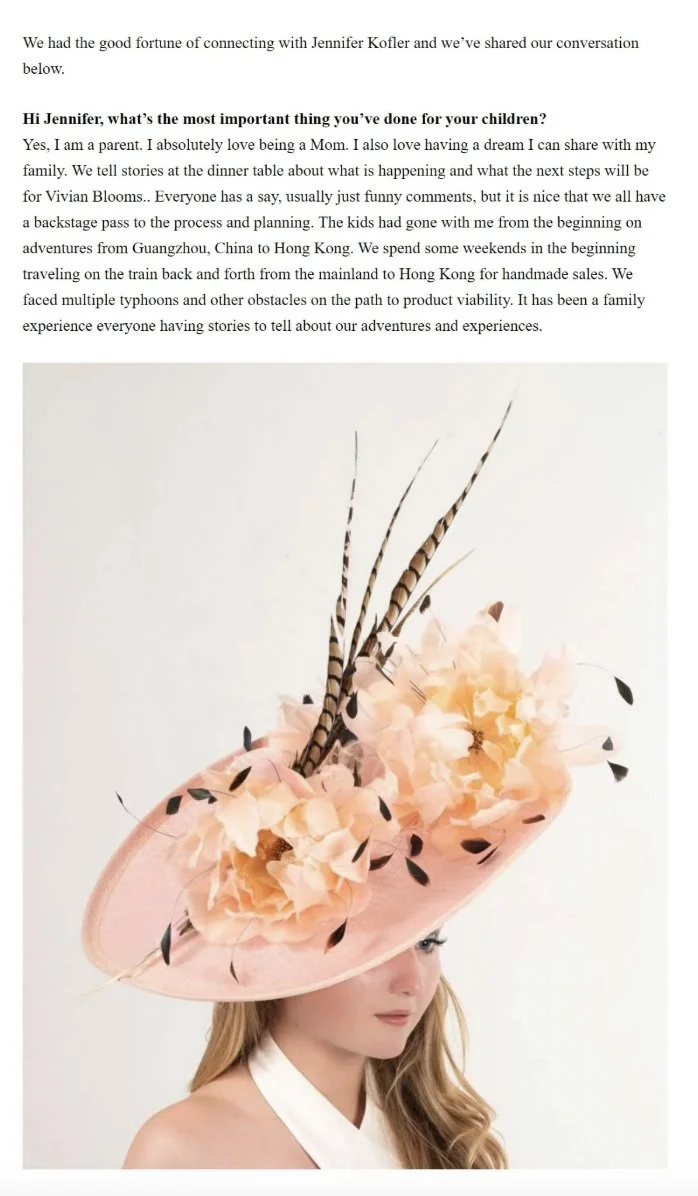 A woman wearing a large, elaborate pink hat decorated with peach-colored flowers, feathers, and black accents.