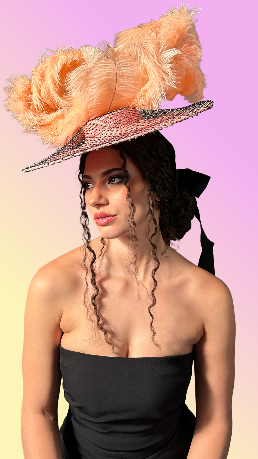 A woman with curly hair wearing a large pink hat with feathers, against a pastel pink and yellow background.