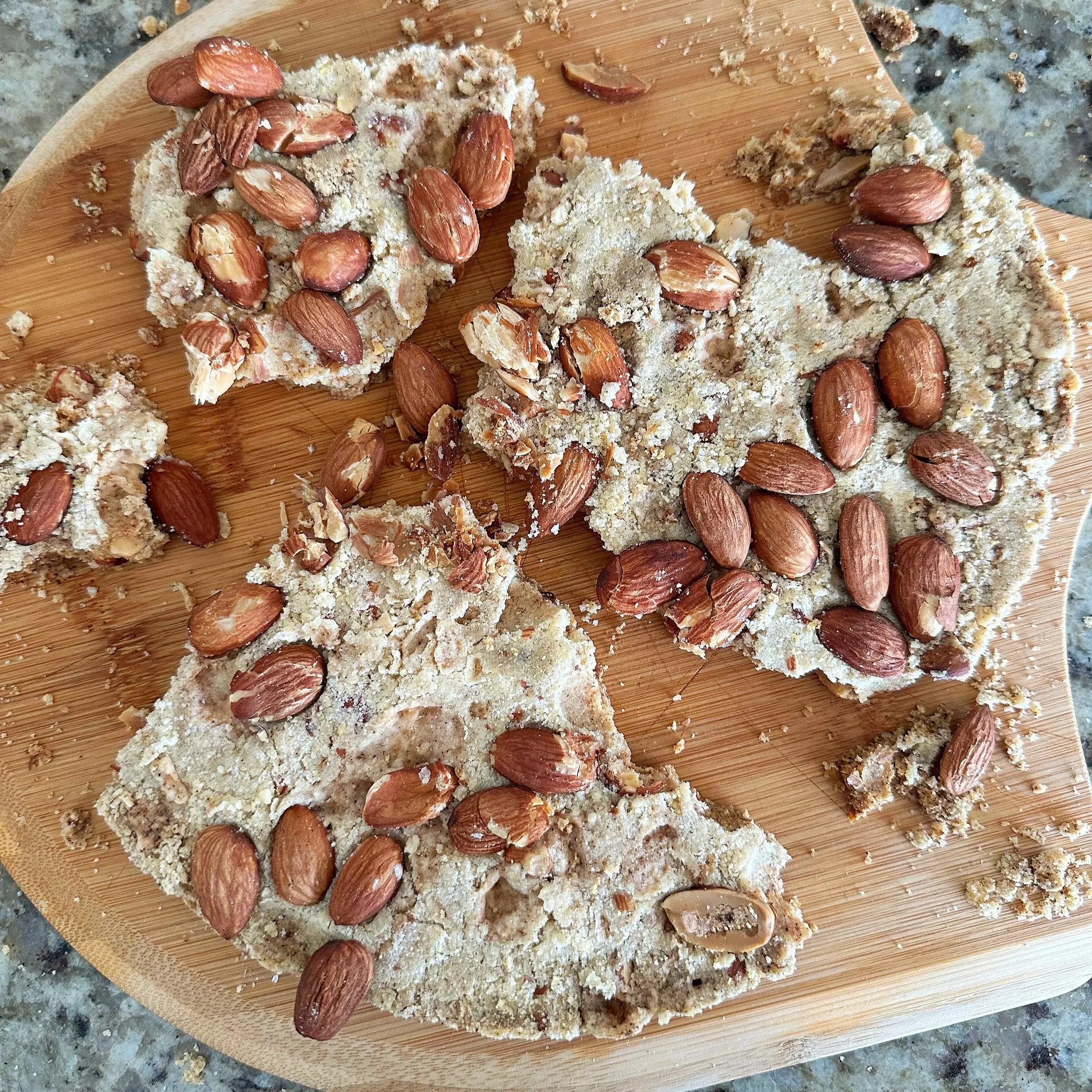 Broken chunks of crumbly cake with almonds on top of a wooden cutting board