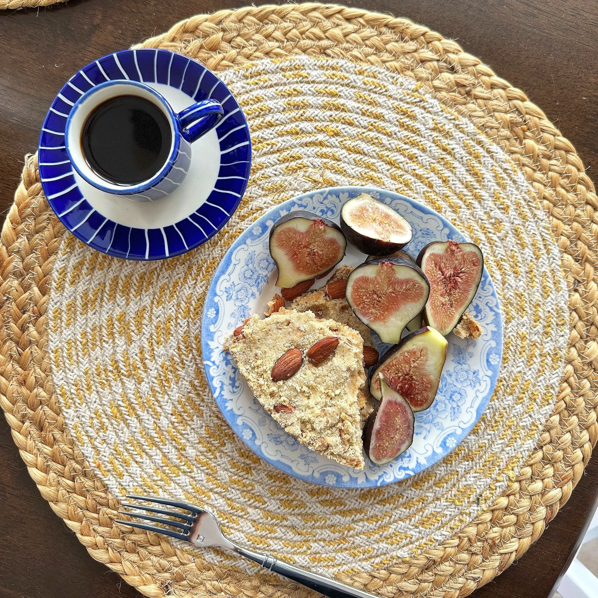 A blue and white cup of espresso beside a plate of coffee cake and sliced figs