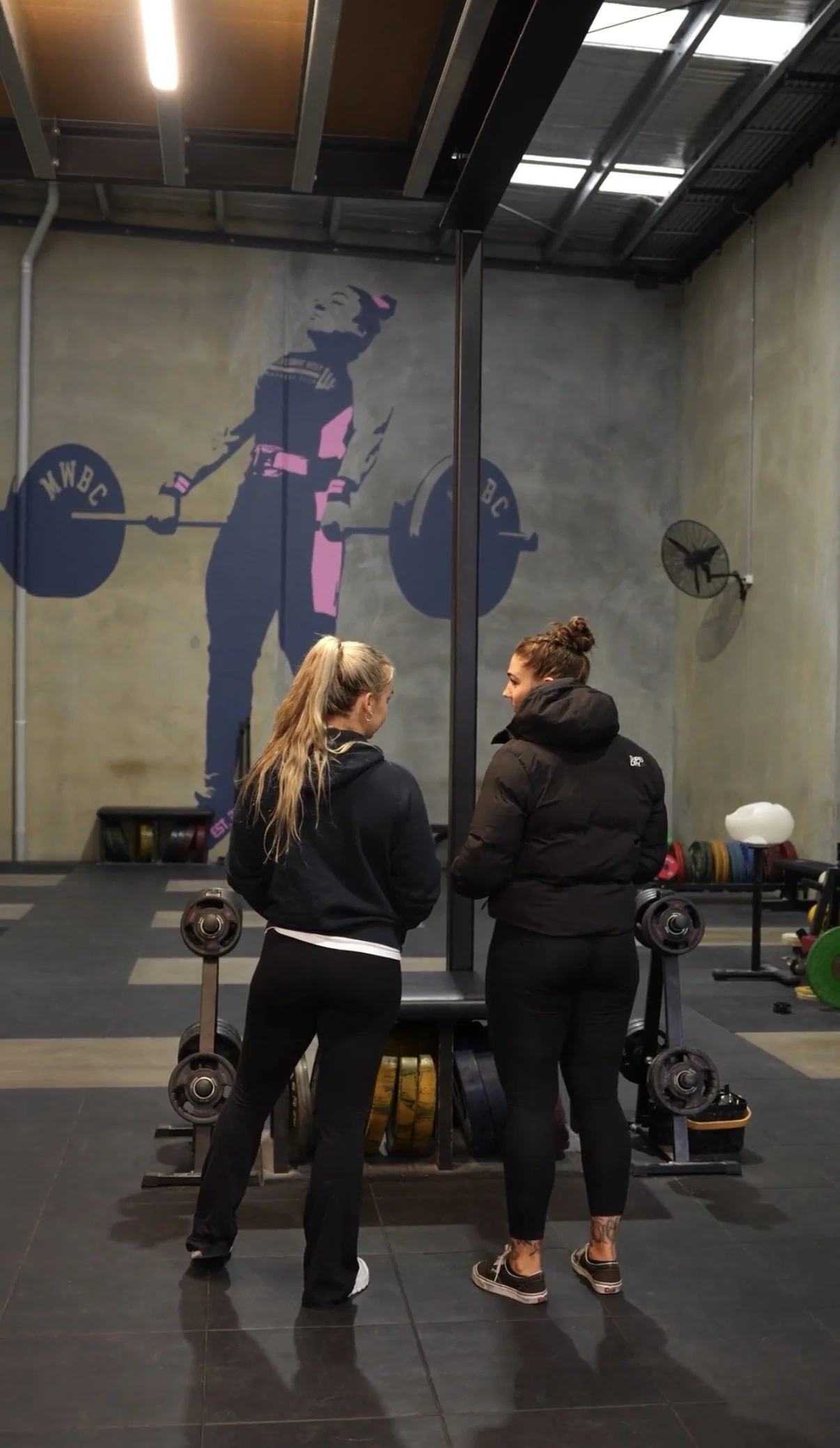 Dr Caity Haniver and her employee talking on the floor of her gym Melbourne West Barbell Club