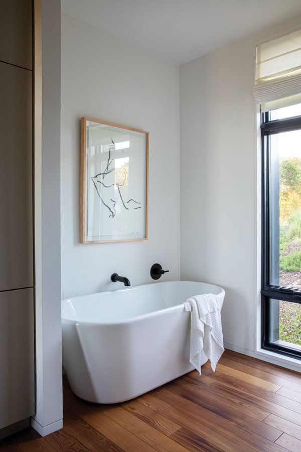  The serene bathroom features a drawing by artist Victor Hugo. The sleek tub and fixtures are part of the Hygge Supply prefab home package. 