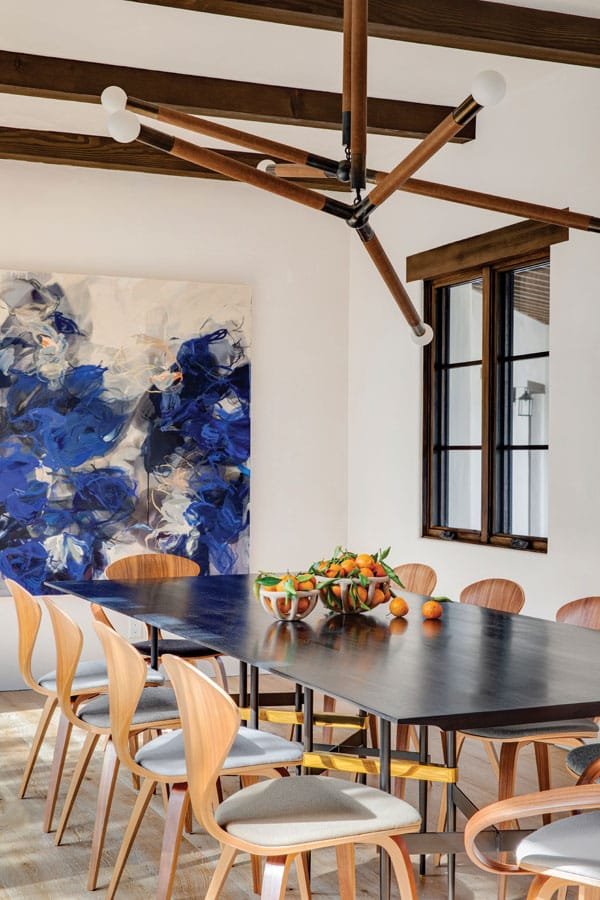  A colorful painting by Canadian artist Bobbie Burgers anchors the dining room. A chandelier by Apparatus illuminates the rectangular dining table surrounded by Cherner dining chairs. 