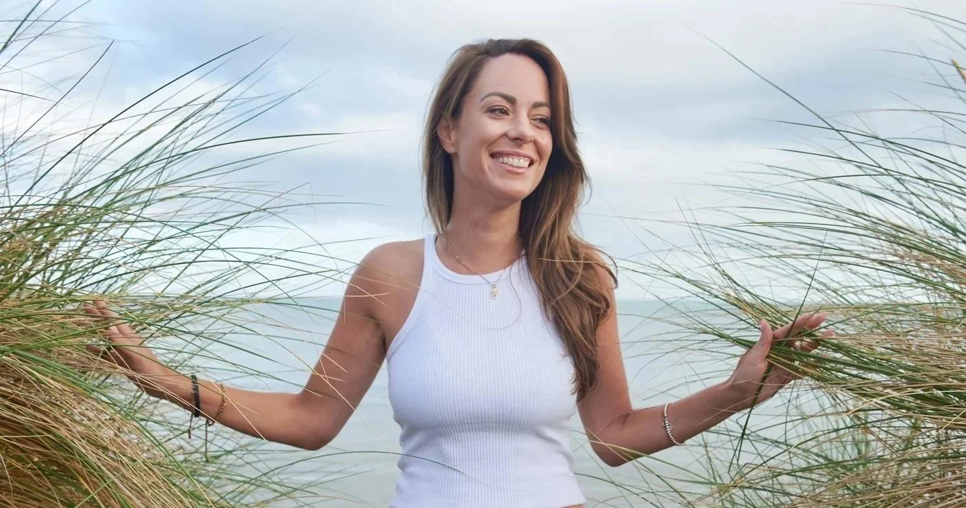 Amanda smiling with her arms open among coastal grasses