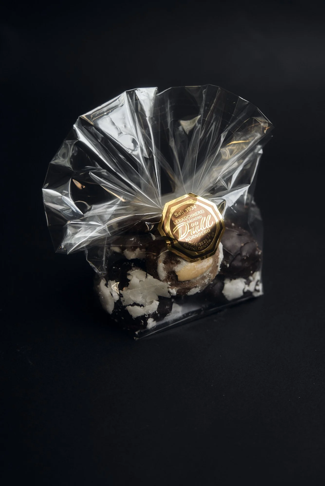 Verpackte Schokoladenpralinen in einer durchsichtigen Plastikverpackung mit einem goldenen Aufkleber, der "Lebküchnerei Drießl Nürnberg" anzeigt, auf schwarzem Hintergrund.