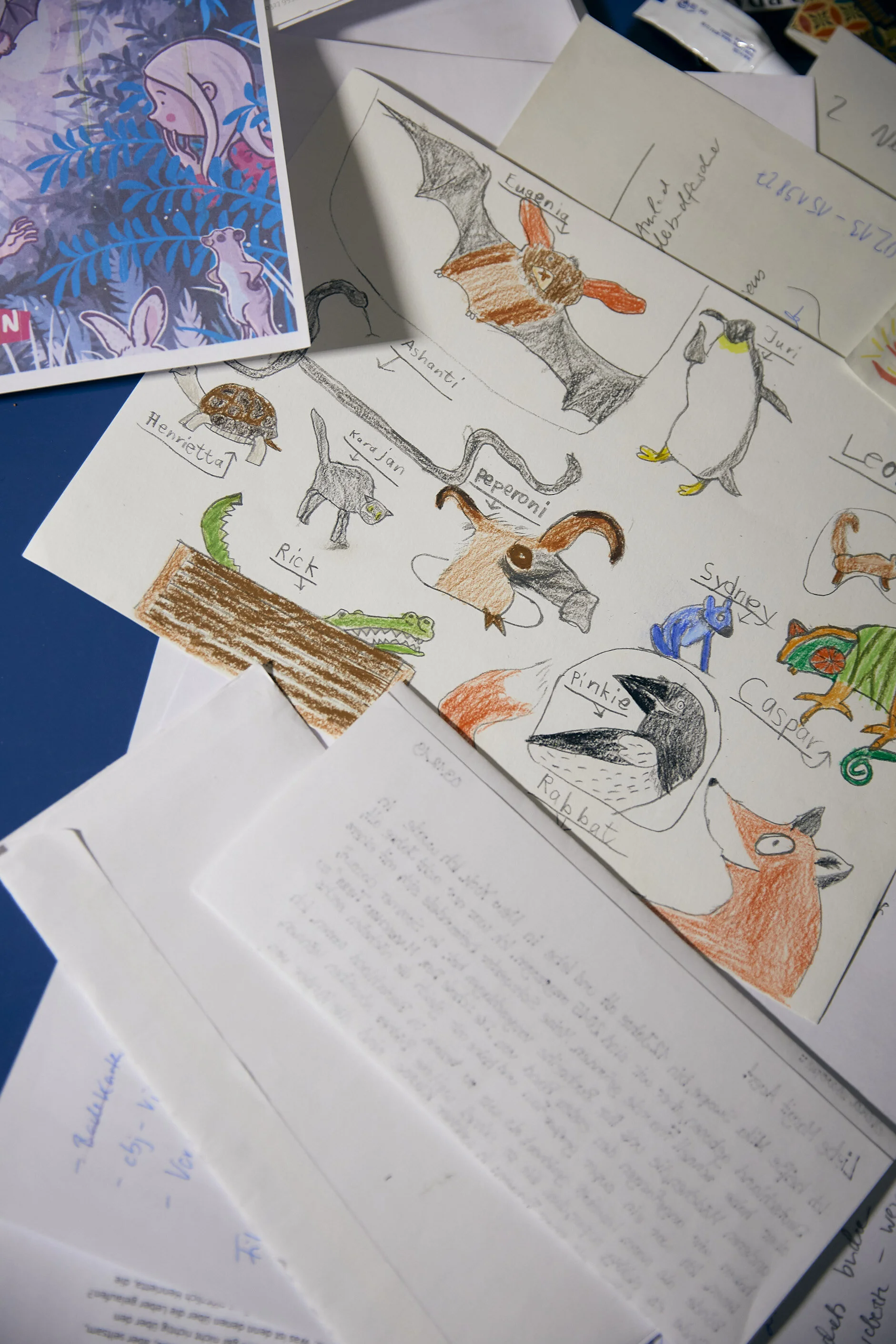 Bunte Zeichnungen von Tieren, darunter eine Fledermaus, ein Pinguin, eine Schildkröte und ein Krokodil, auf einem Tisch mit verstreuten Blättern und Dokumenten.
