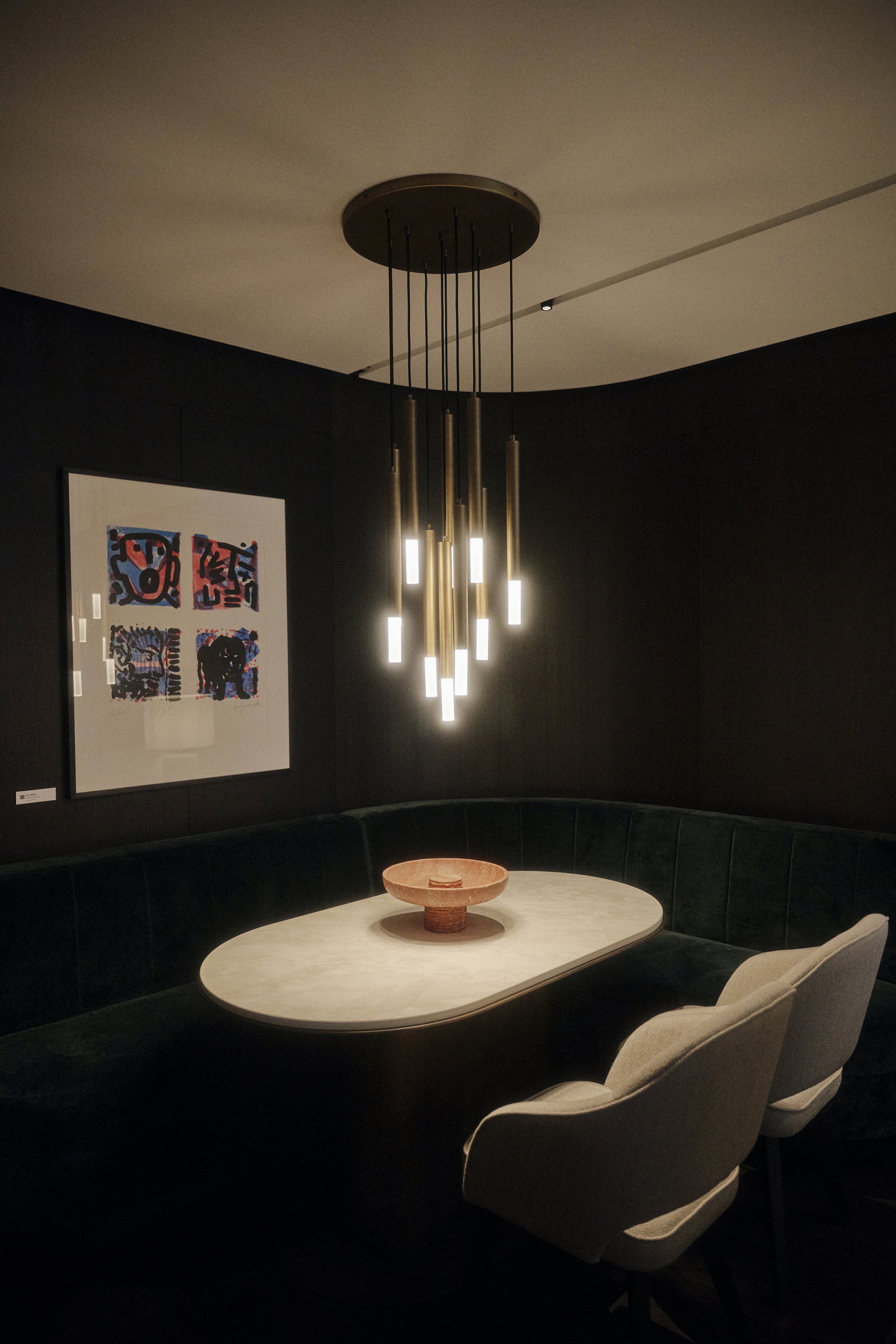 Elegantes Esszimmer mit modernem Kronleuchter, ovalem Tisch, zwei Polsterstühlen, grüner Bank und abstraktem Kunstwerk an der Wand.