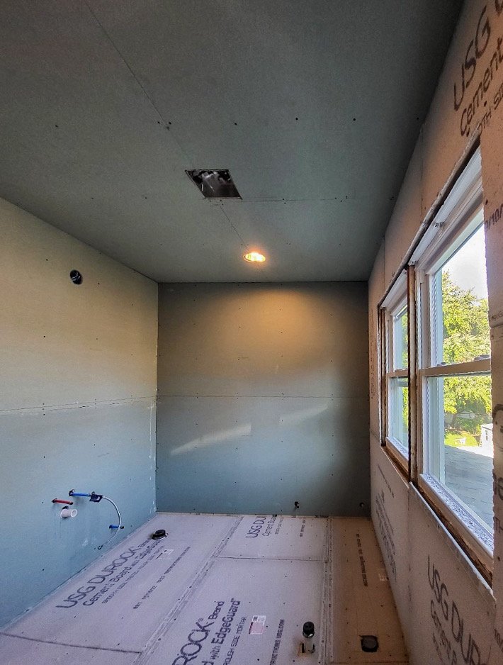 Interior of a room under construction with drywall installed and a window on the right wall.
