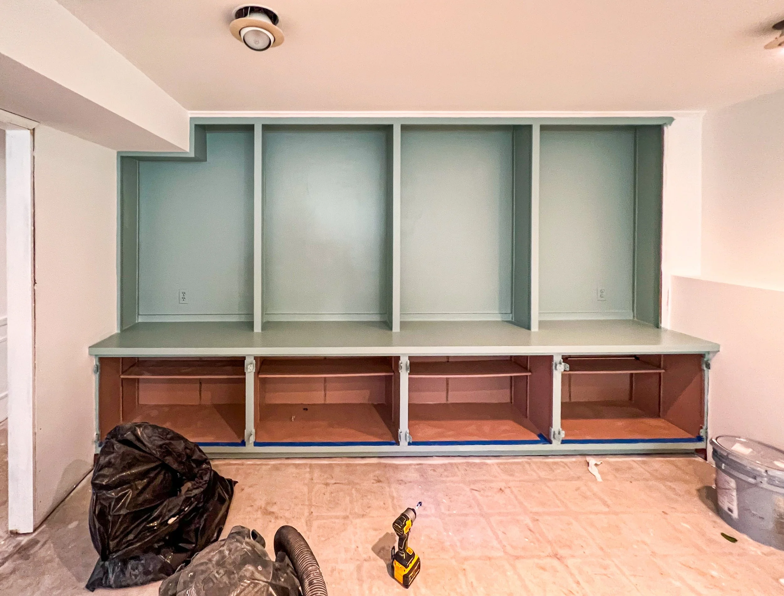  unfinished built-in shelving unit with upper section painted light blue and lower section with open compartments, in a room under renovation with tools and construction materials on the floor.