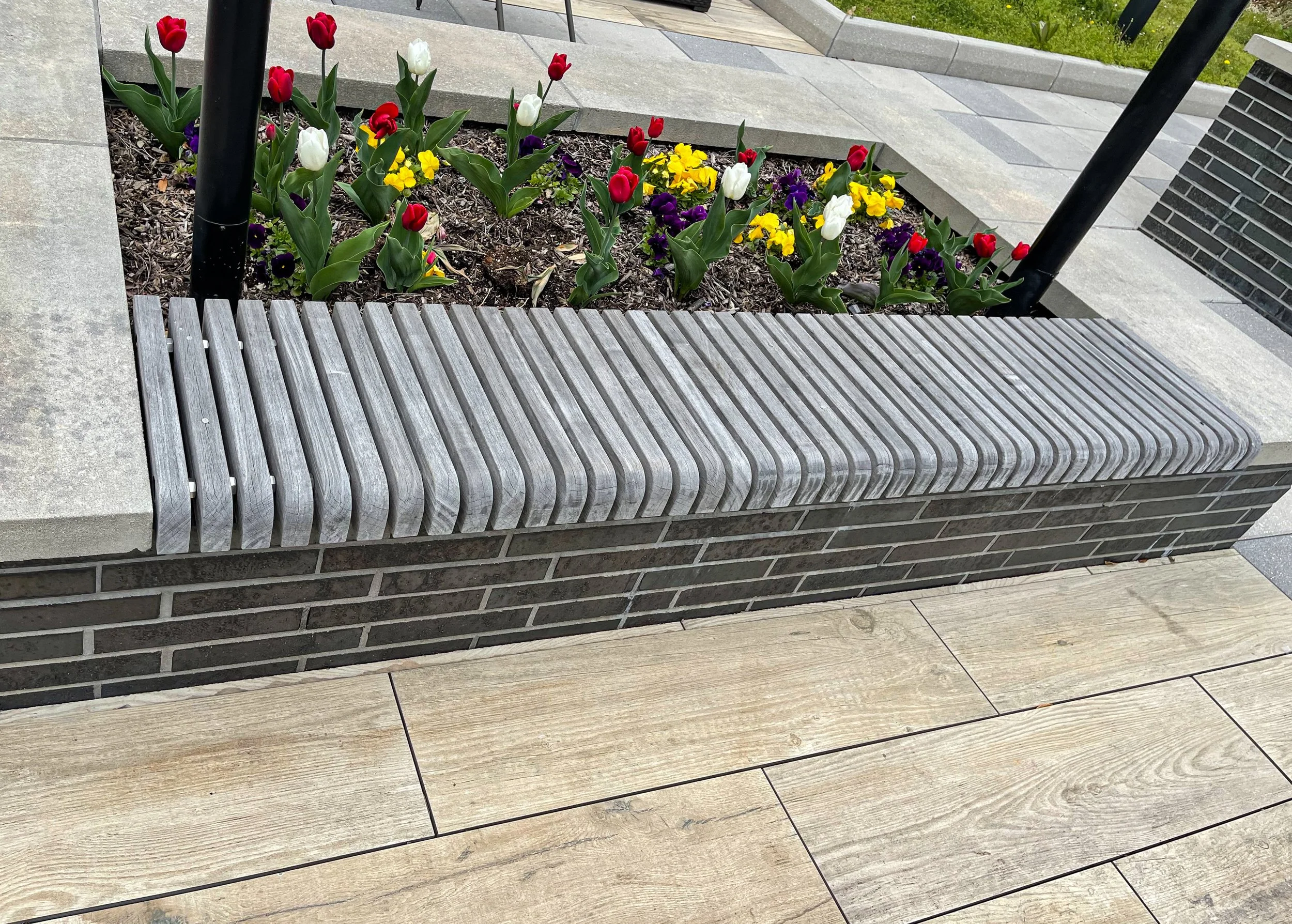 A flowerbed with colorful tulips and pansies next to a staircase and a wooden bench in an urban setting.