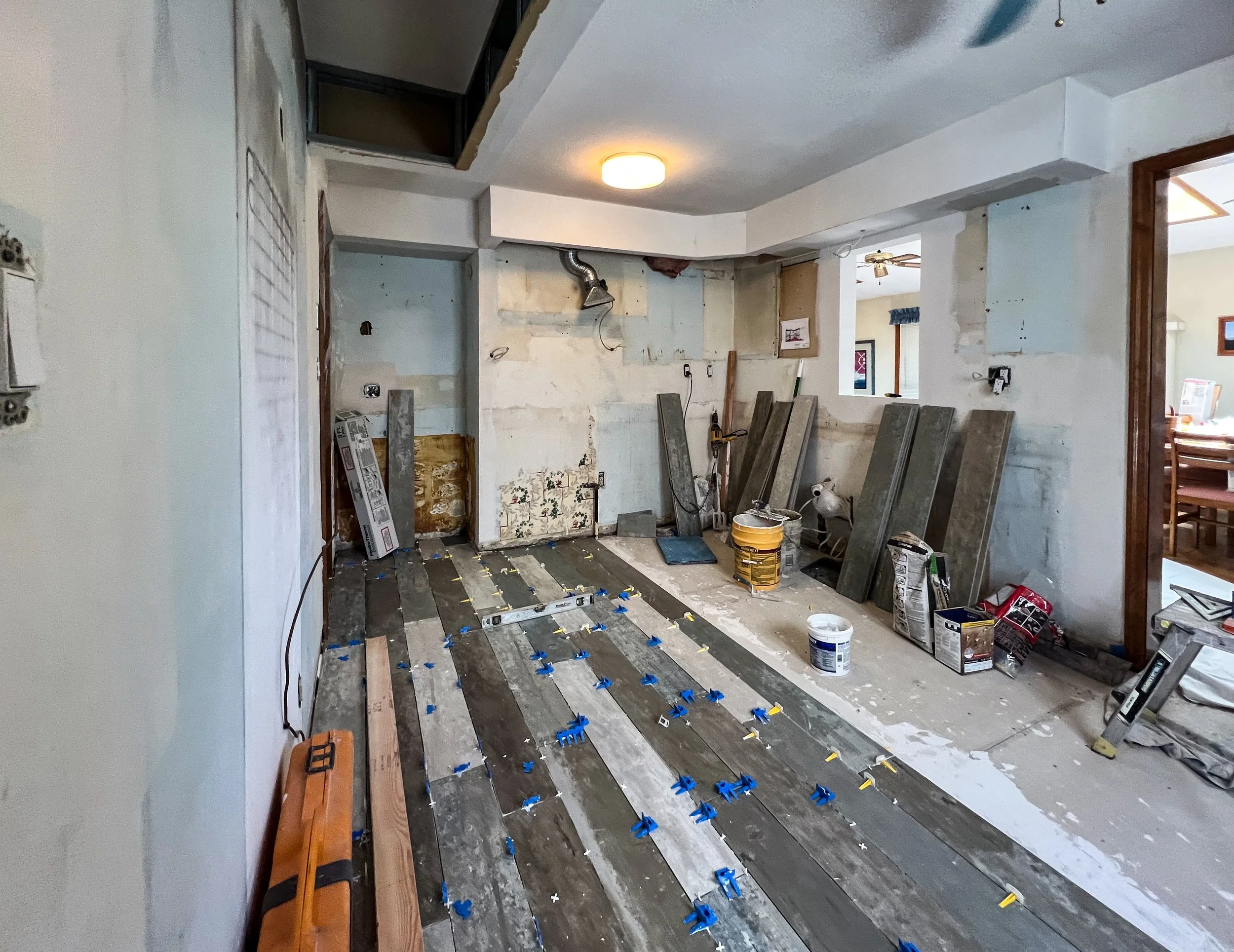 Room under renovation with floor tiles being installed, visible construction materials, and tools scattered around.