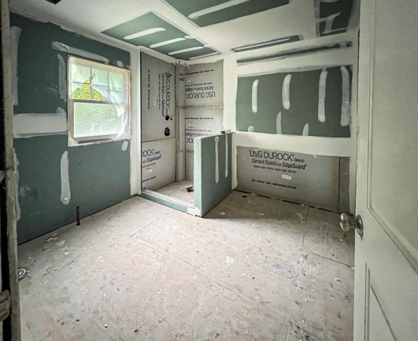 A room under construction with unfinished drywall, a window covered with plastic, and an open doorway.