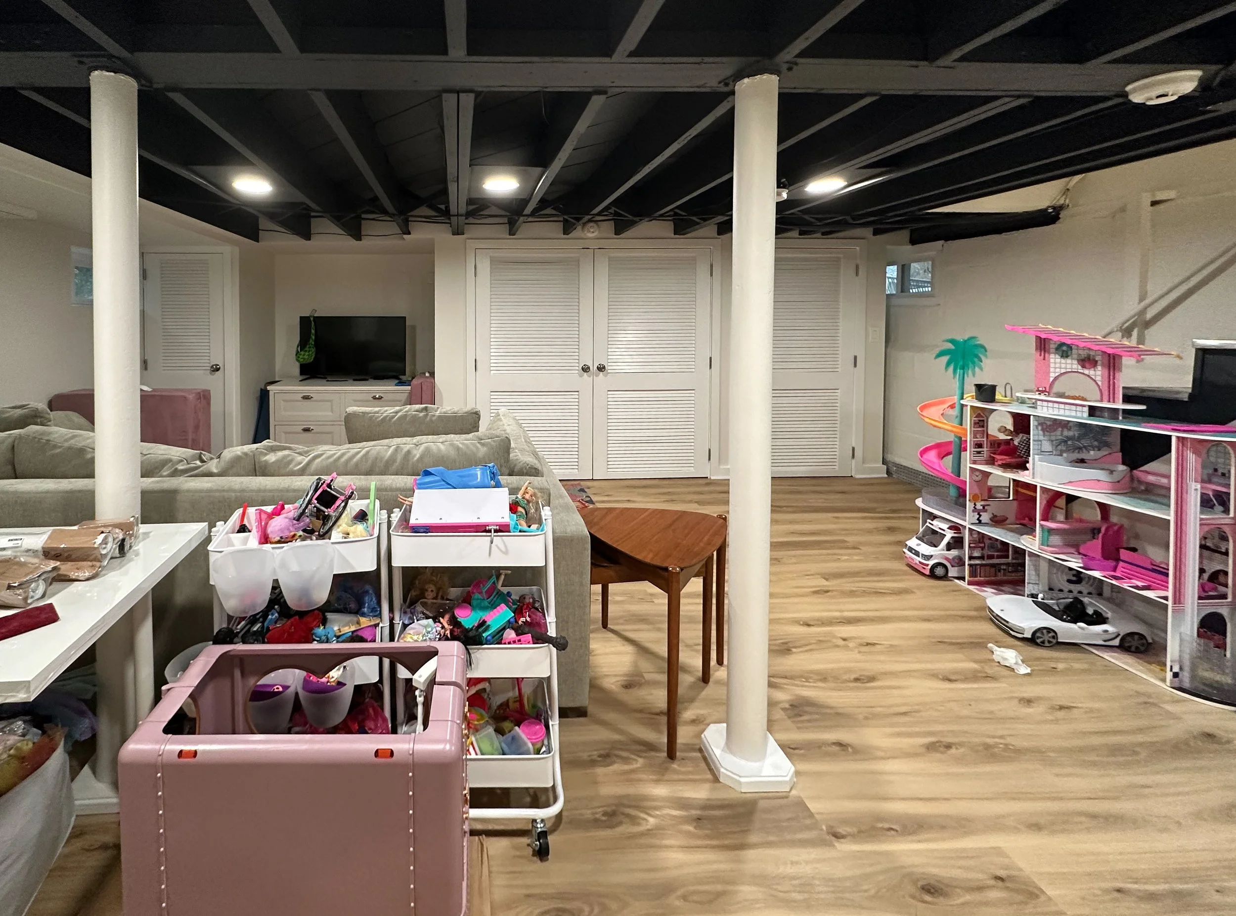 Basement playroom with toys, a TV, couches, and storage shelving.