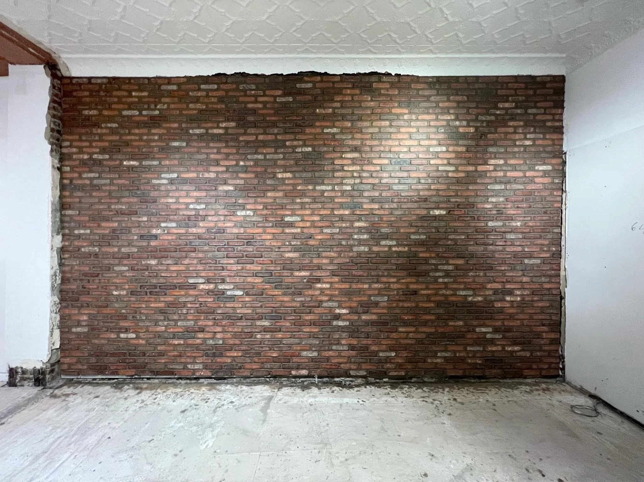 Interior wall with exposed brick in a room under renovation, with drywall and unfinished flooring.