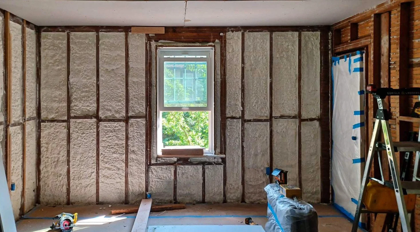 Room under renovation with insulated walls, window, ladder, and construction tools.