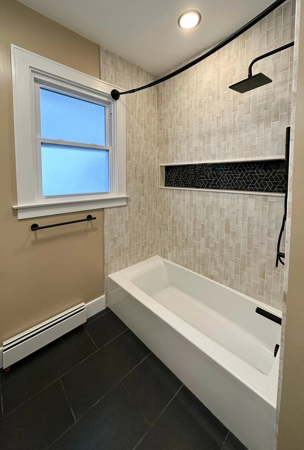 Bathroom with a tiled shower, black showerhead, and a window with frosted glass.