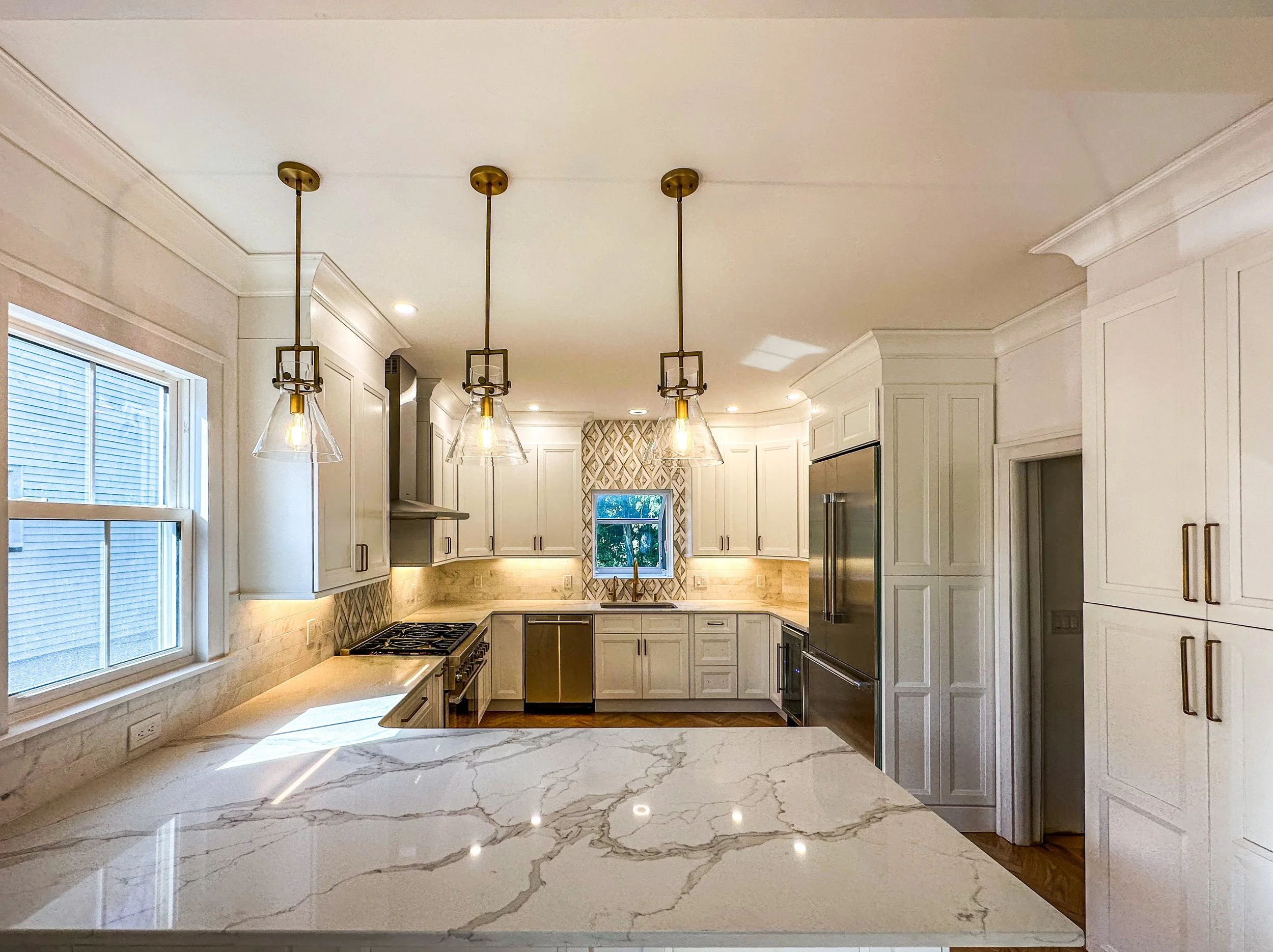 Modern kitchen with white cabinets, marble countertop island, stainless steel appliances, pendant lights, a window, and a patterned tile backsplash.