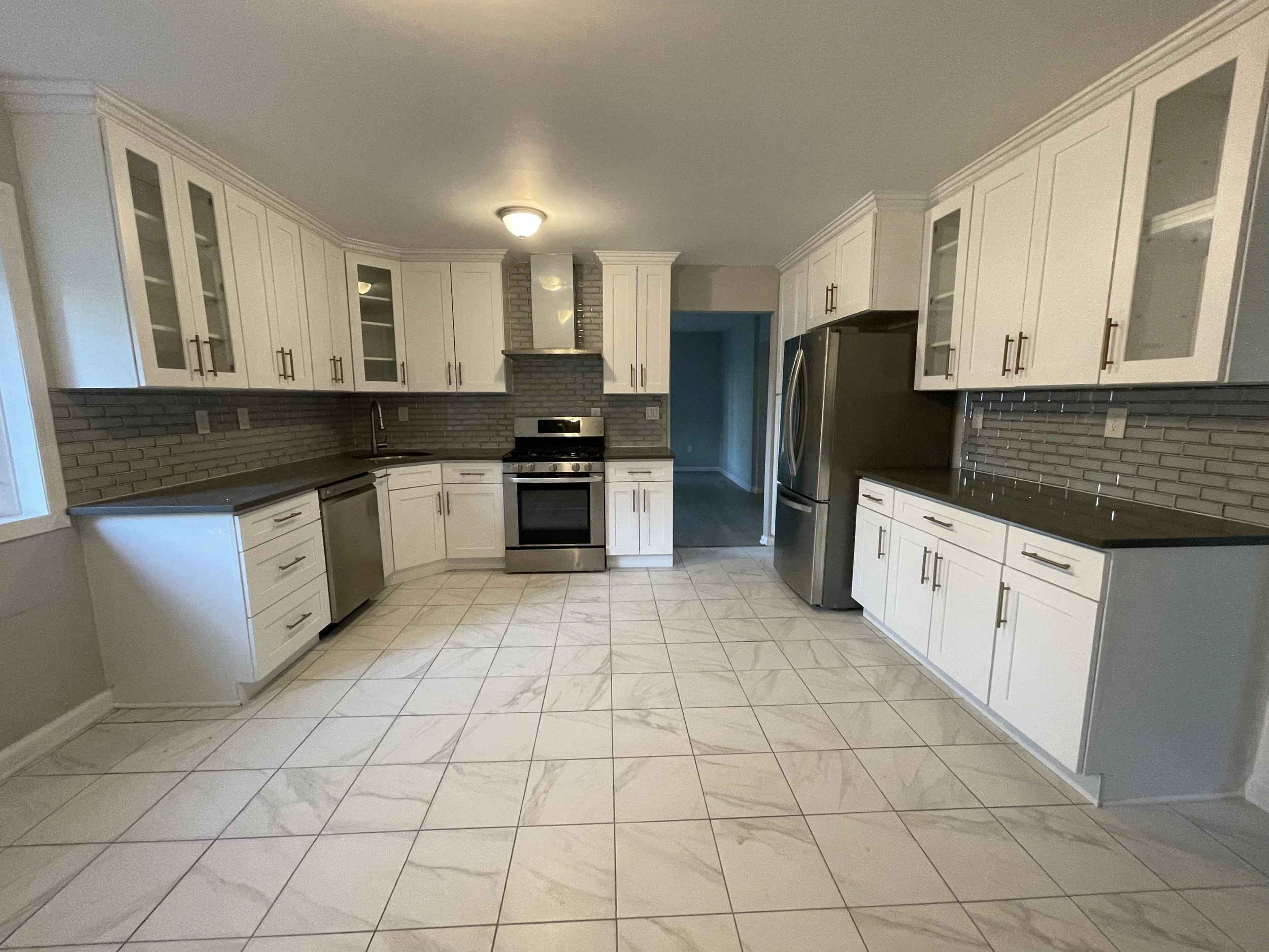 Modern kitchen with white cabinets, gray countertops, stainless steel appliances, a brick backsplash, and large tiled floor.
