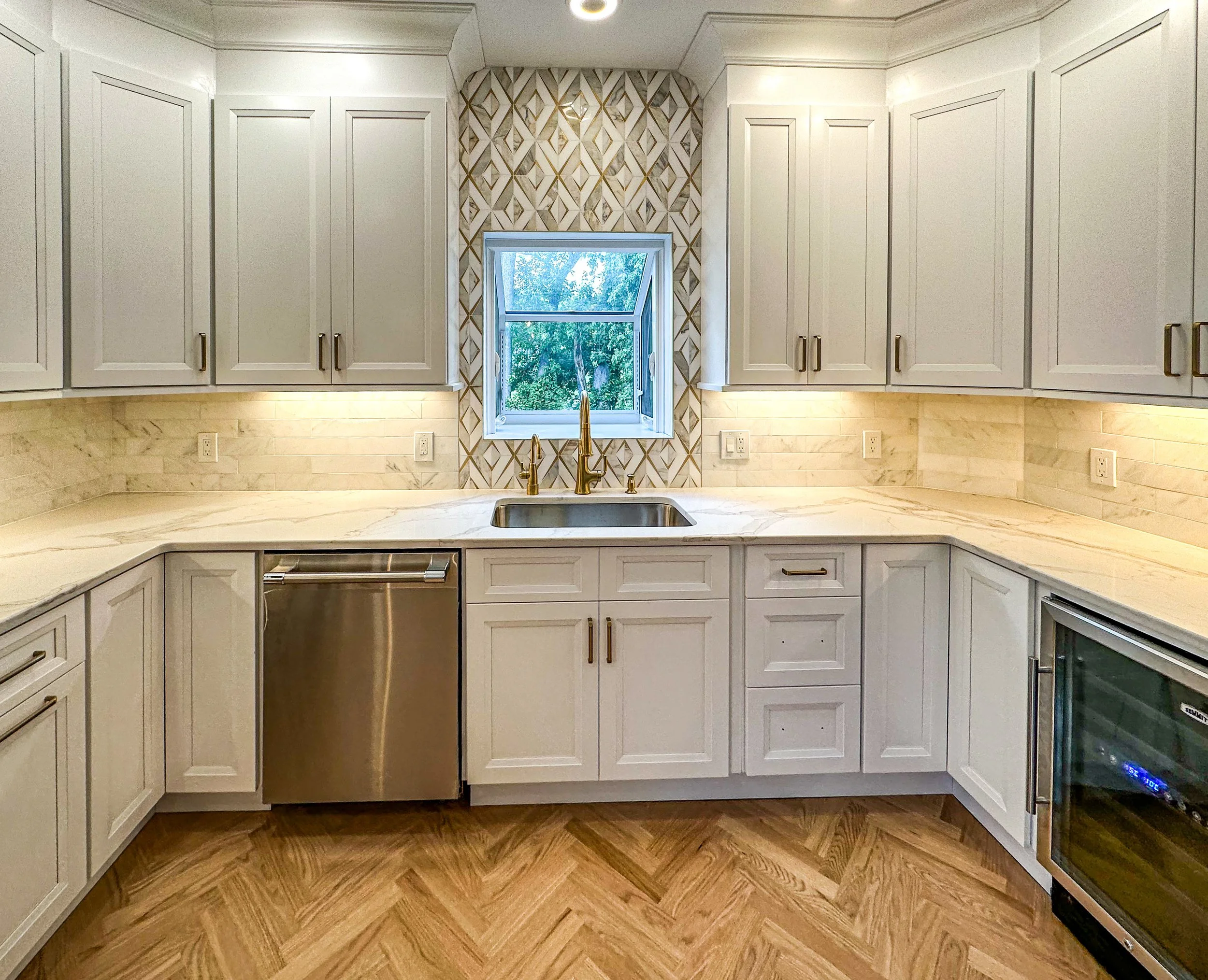 Modern kitchen with white cabinets, marble countertops, a window above the sink, and stainless steel appliances.