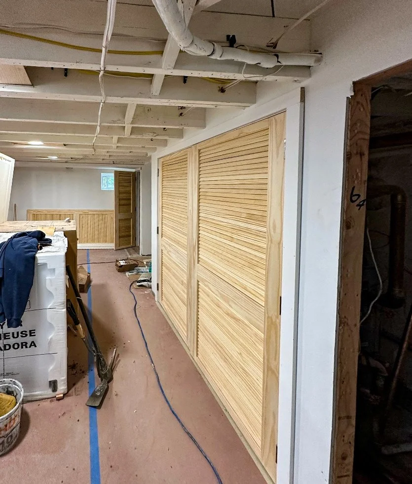 Interior view of a basement under construction with unfinished ceiling and new wooden sliding closet doors.
