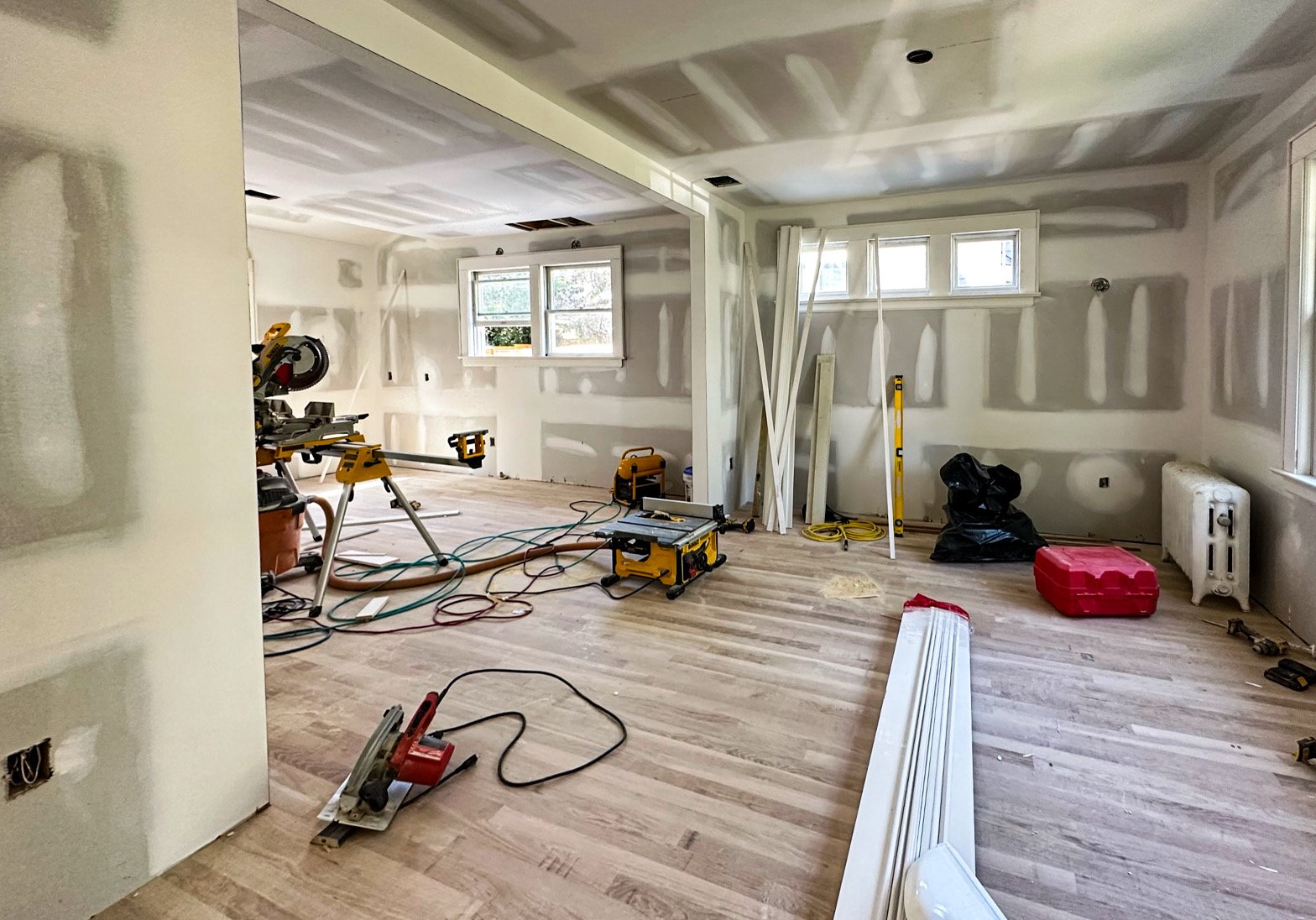 Interior of a room under renovation with drywall installation, construction tools, and materials scattered on the wooden floor.