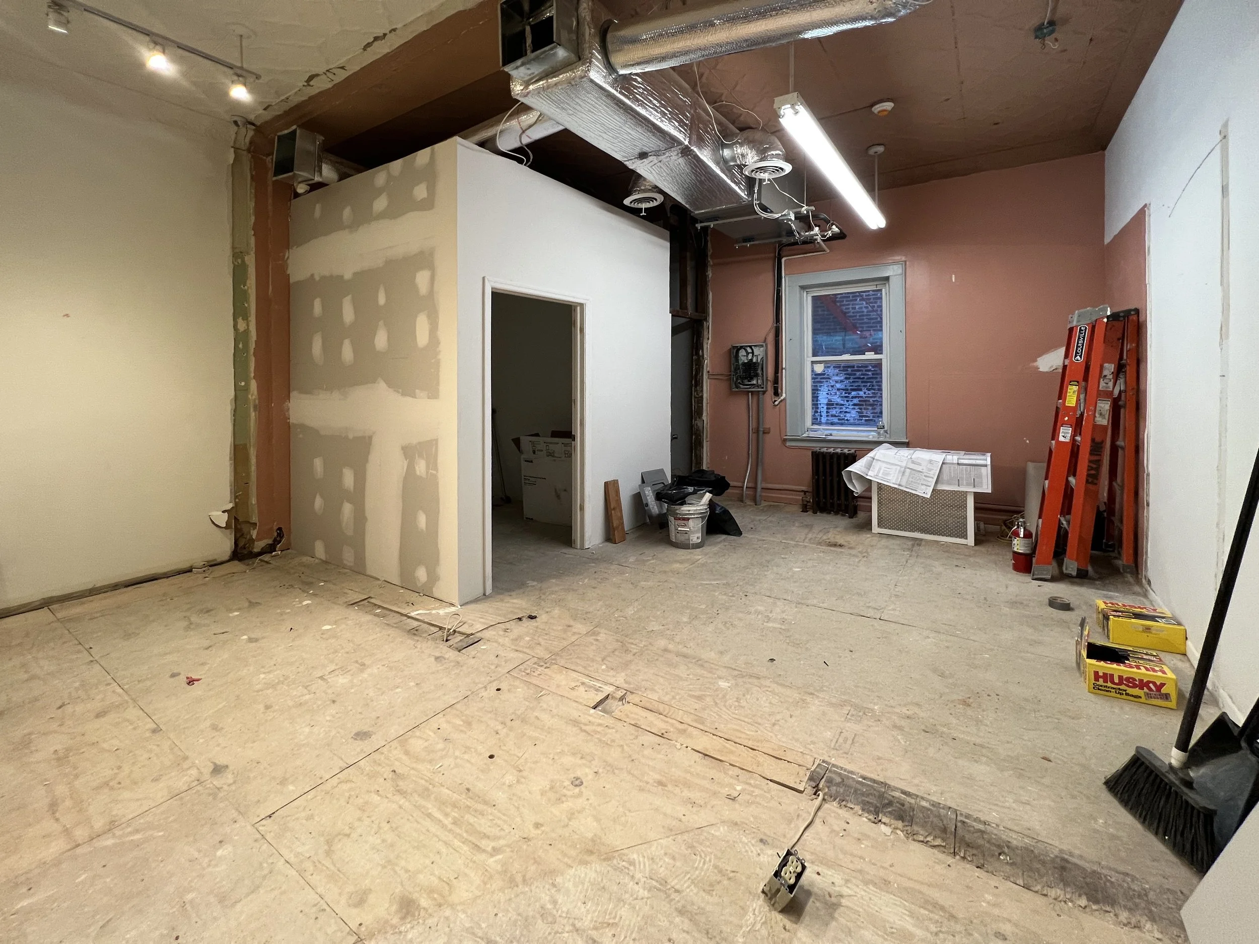 Room under renovation with drywall installation, exposed ductwork, ladder, and construction tools. A window shows snow outside.