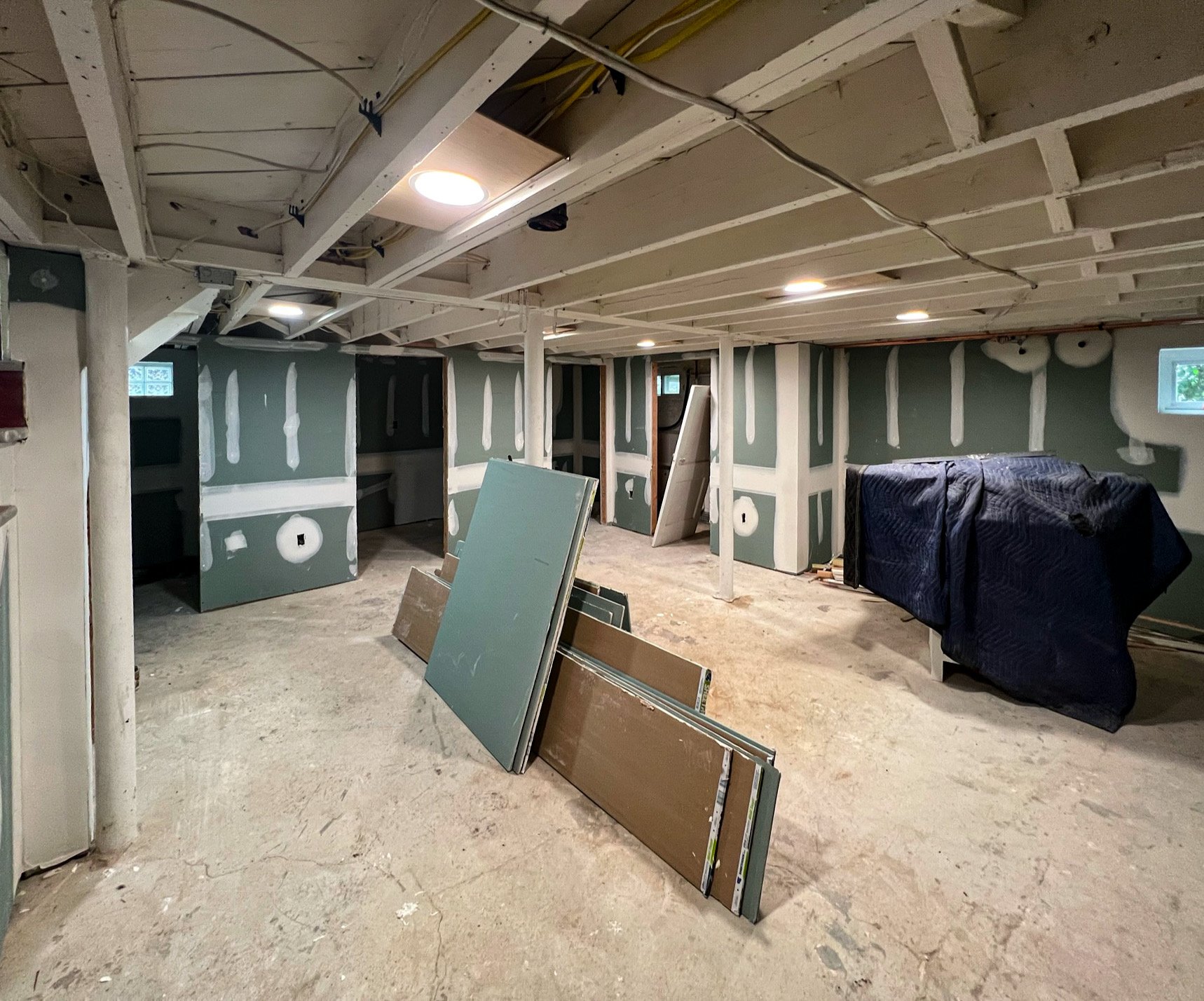 Interior view of a basement under construction with drywall partly installed, construction materials on the floor, and a covered object on a stand.