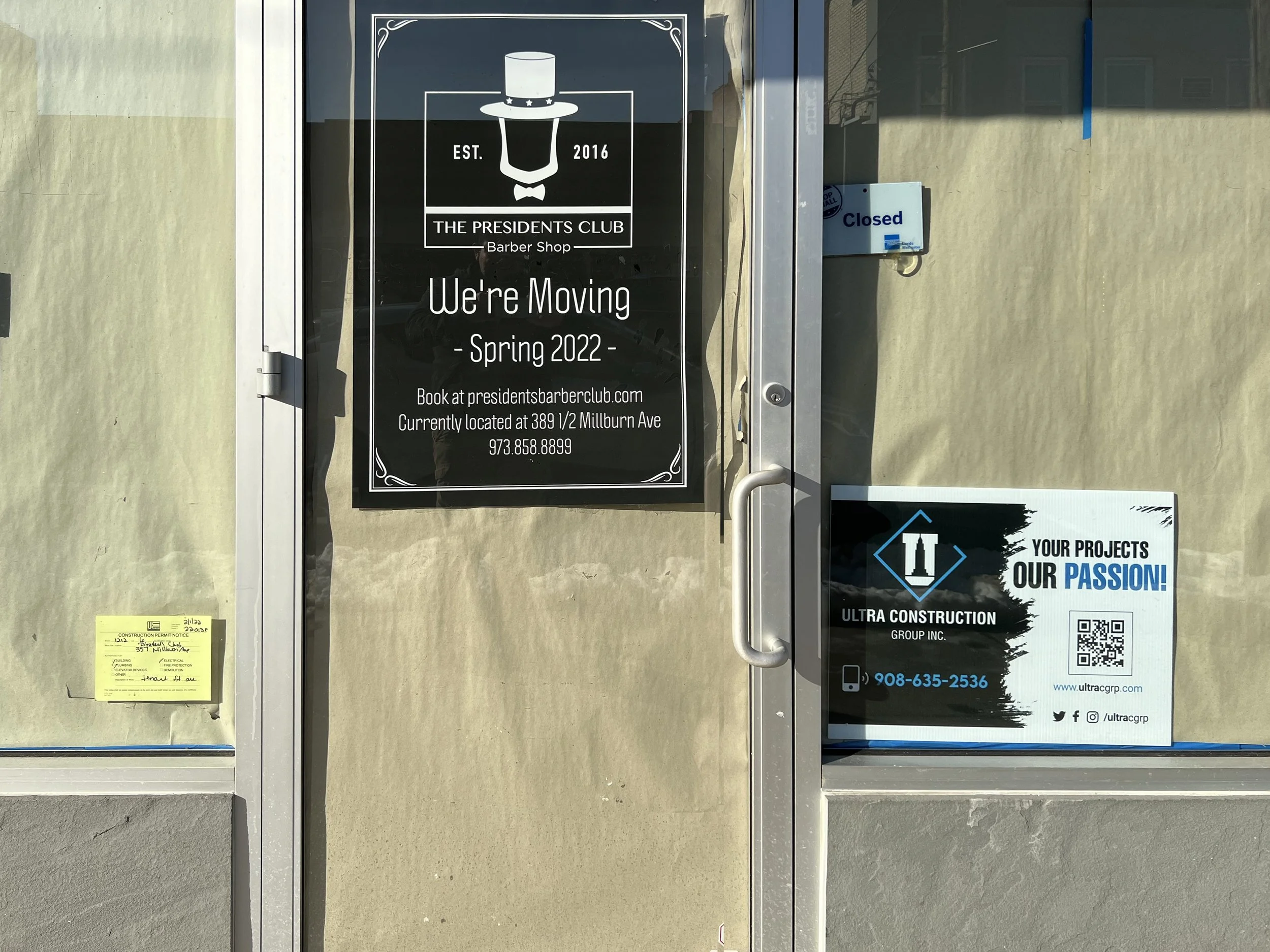 Sign on door announcing the business is moving to a new location in spring 2022, with contact details. A smaller sign indicates the business is closed.